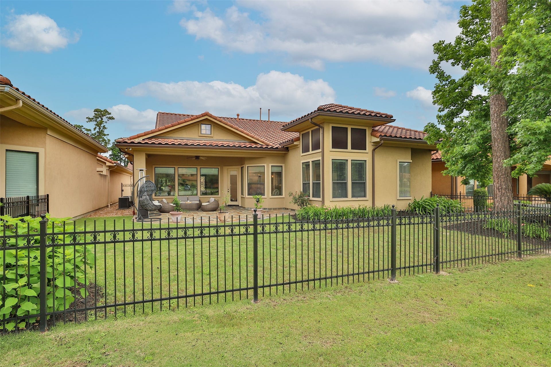 Charming home with a Mediterranean-style exterior, featuring a terracotta roof and large windows. The backyard is fenced, landscaped, and includes a cozy patio area perfect for outdoor relaxation.