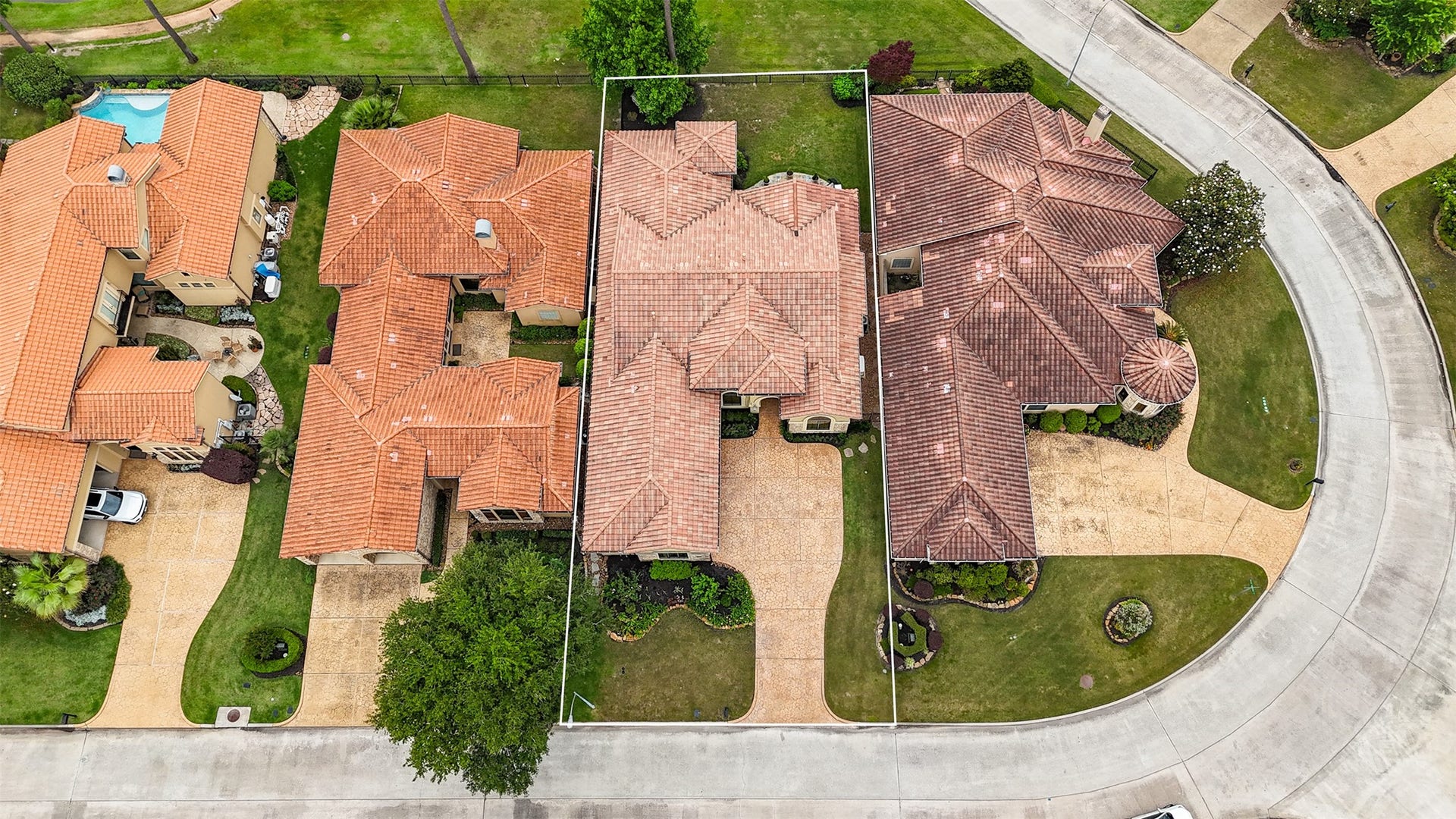 Aerial view of a charming single-story home with a tiled roof, situated in a well-maintained neighborhood. It features a spacious driveway, a small front yard with landscaping, and is flanked by similar style homes. Ideal for those seeking a cozy suburban setting.