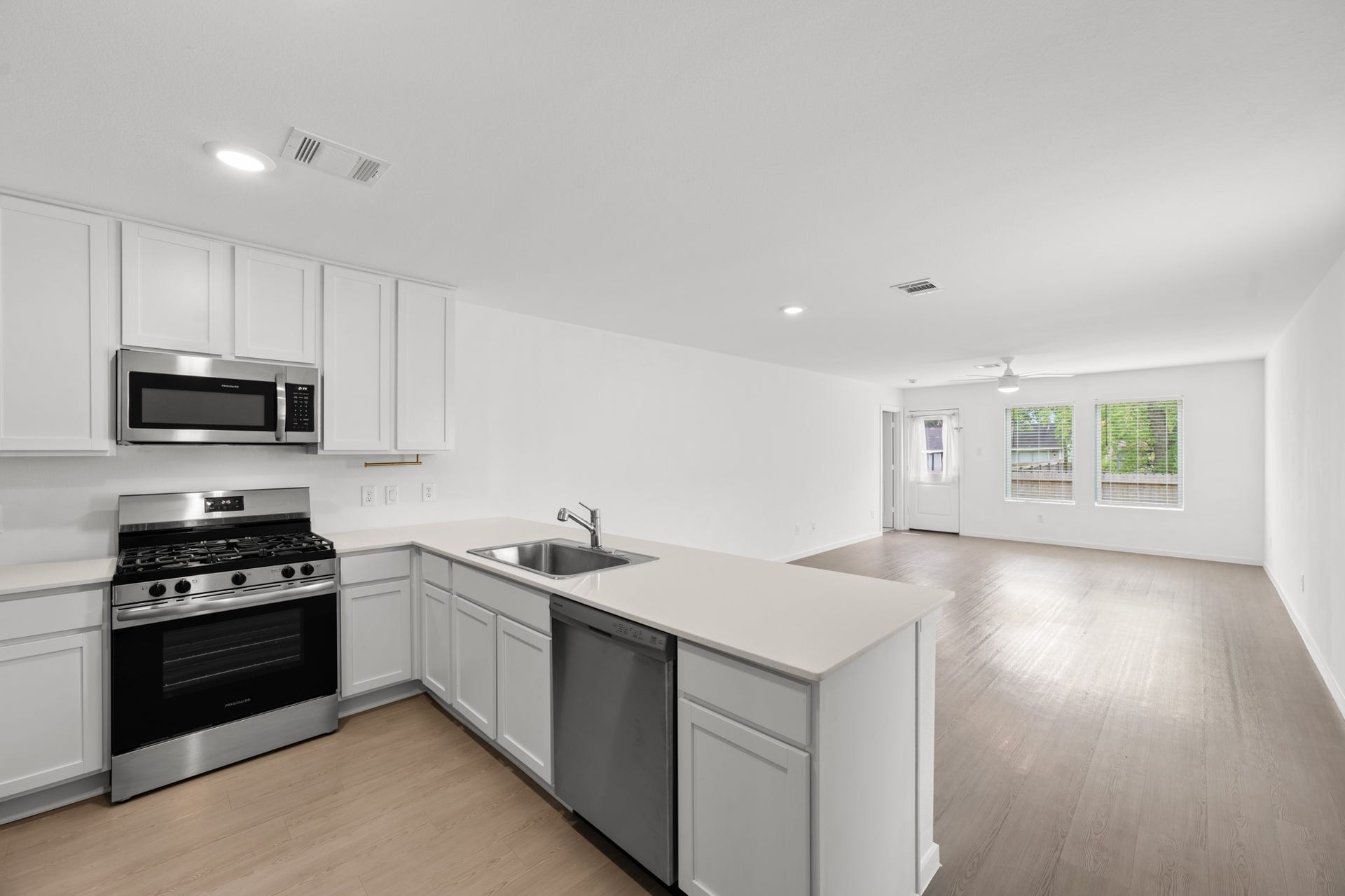 Open-concept kitchen flows directly into the living area, with a spacious peninsula creating a natural connection between the two spaces. Stainless steel appliances, white cabinetry, and recessed lighting provide a clean, contemporary look.