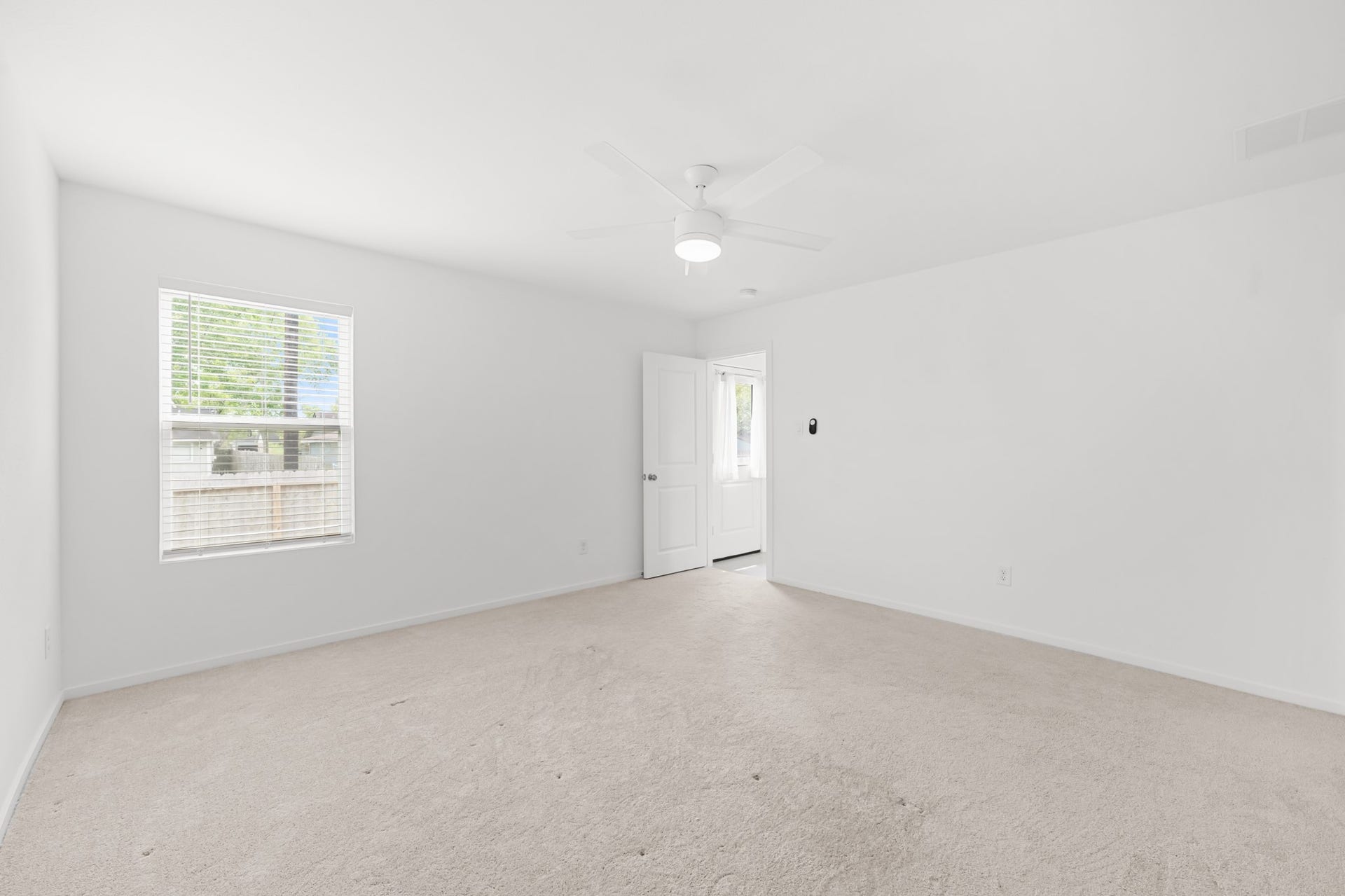 Spacious primary bedroom features neutral carpeting, a ceiling fan, and a large window that brings natural light into the room.