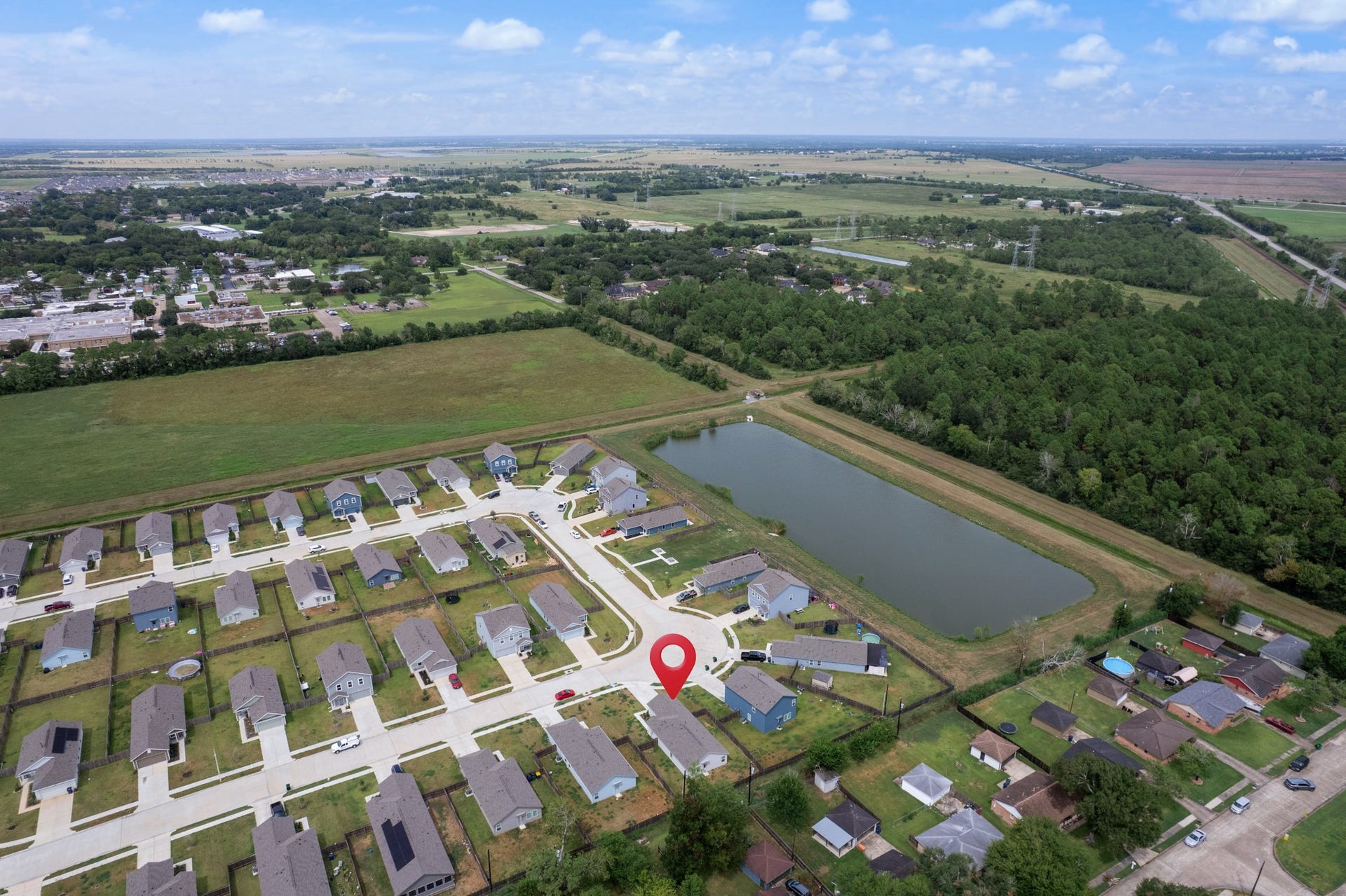Wide aerial view showcases the neighborhood layout, nearby pond, and surrounding green space, with the property clearly marked.