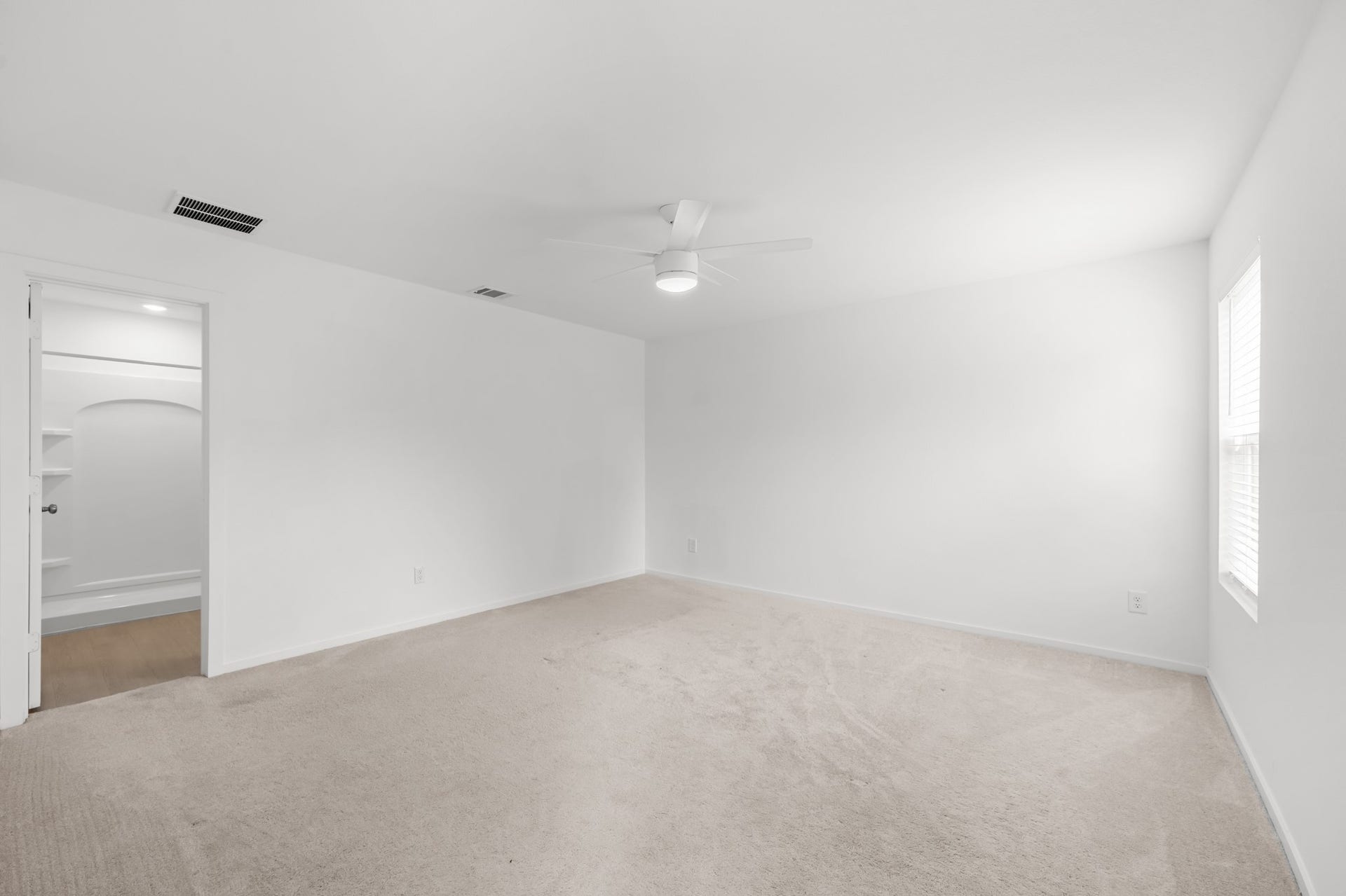 Spacious primary bedroom features soft carpeting, neutral finishes, a ceiling fan, and natural light from a side window.