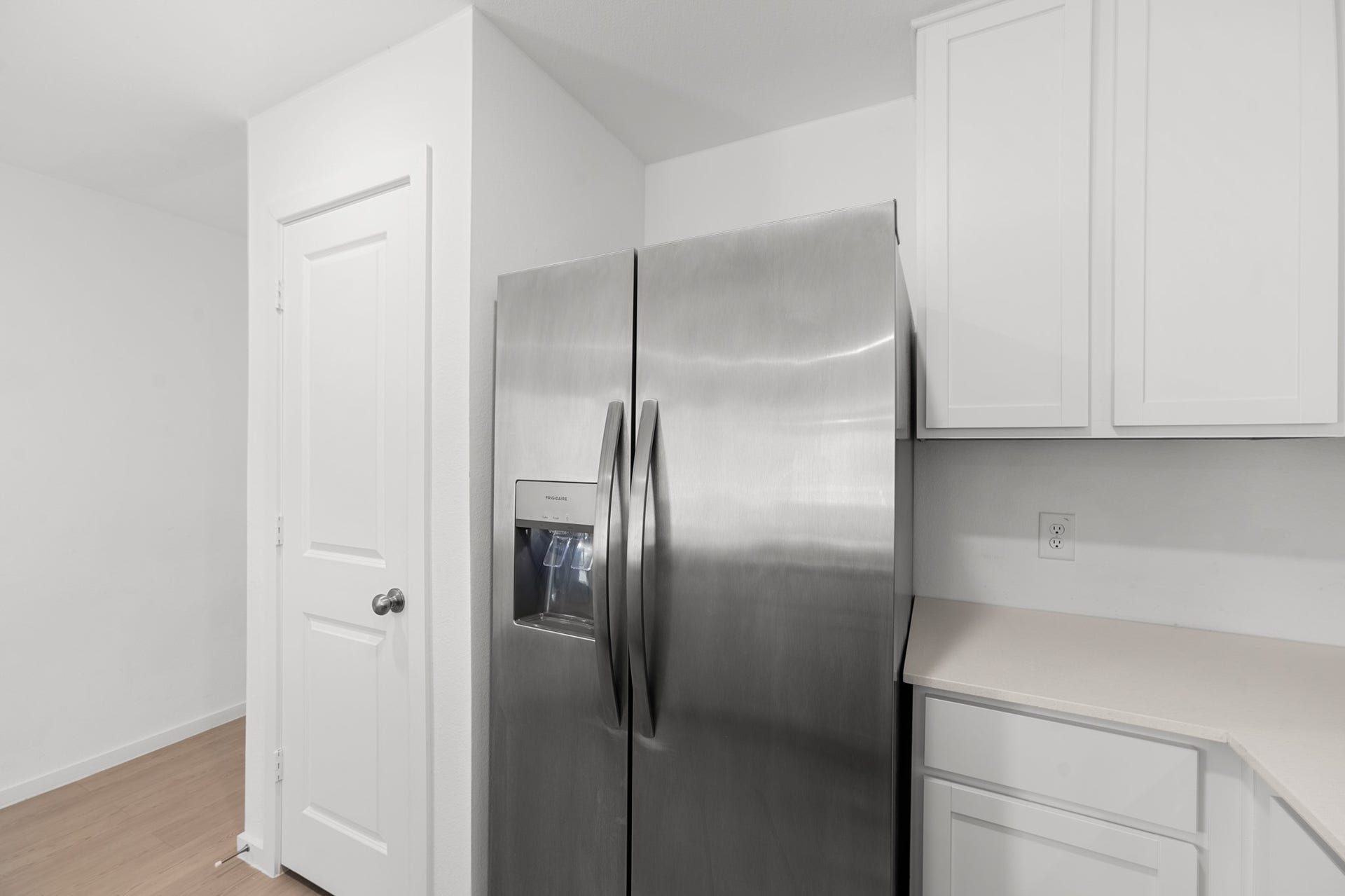 Stainless steel side-by-side refrigerator with in-door water and ice dispenser complements the crisp white cabinetry and adjacent countertop space.