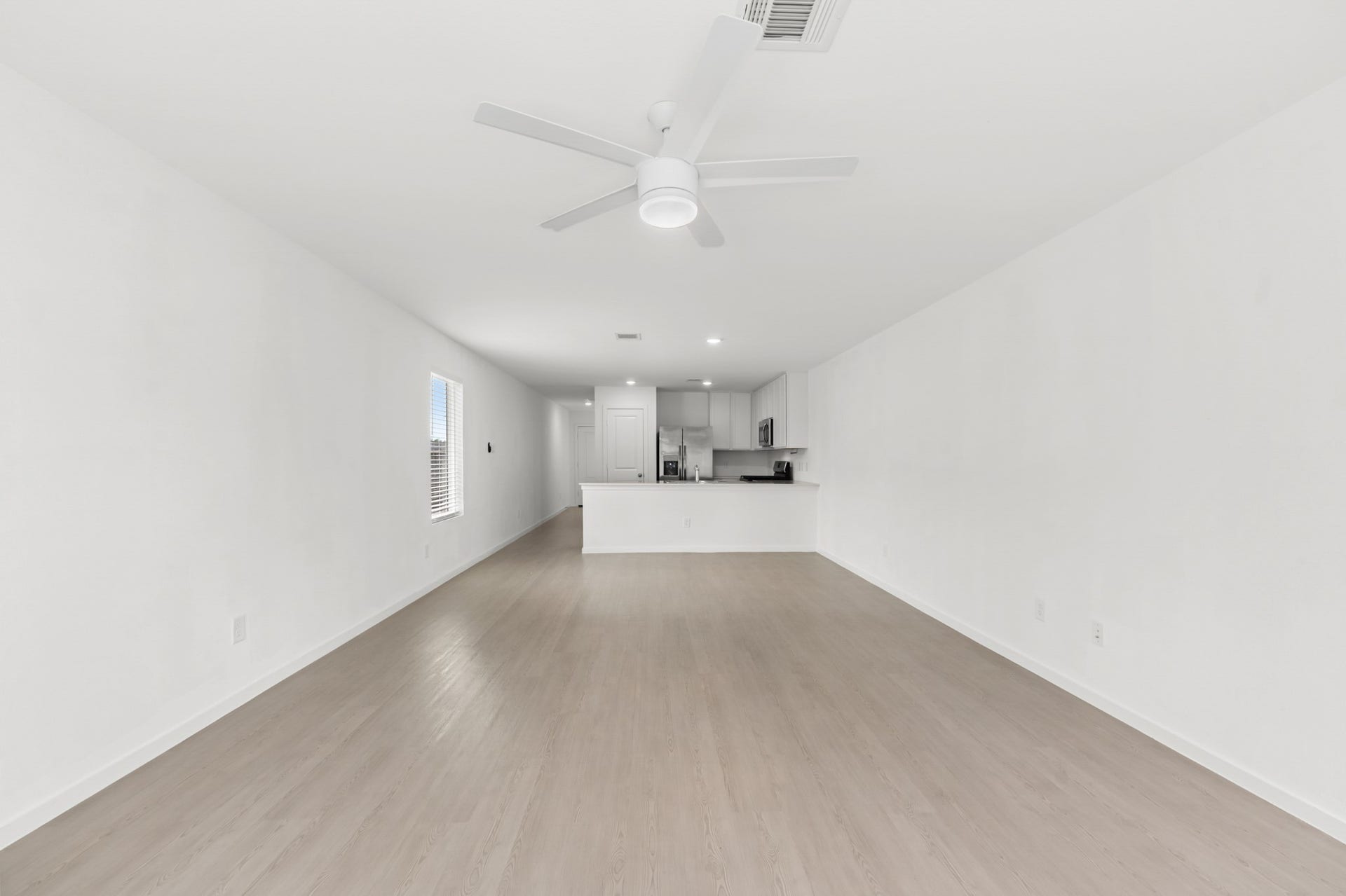 Spacious living room offers a long, open footprint with light-toned flooring, a ceiling fan, and a direct sightline to the kitchen.