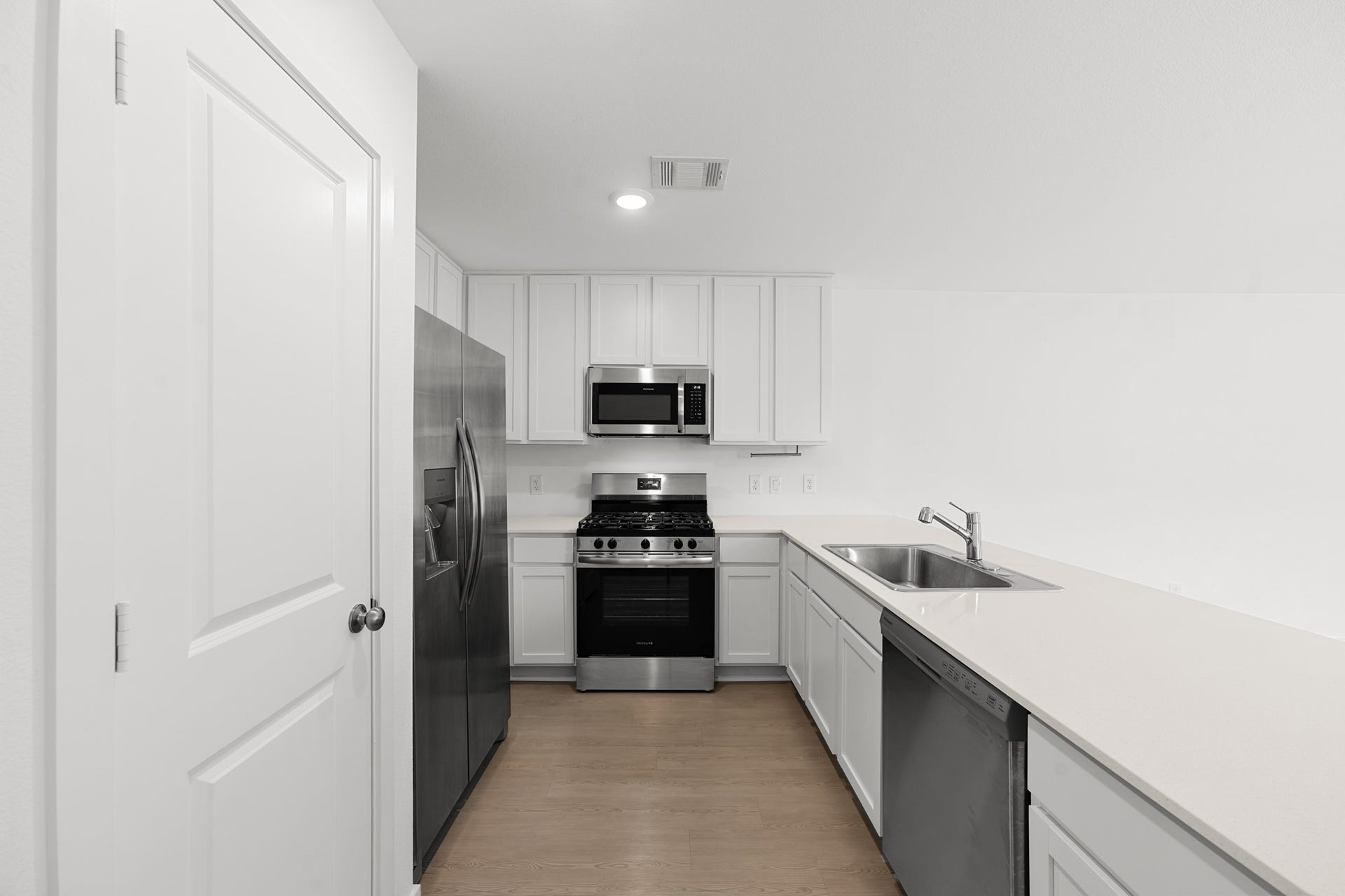 Another view highlights the kitchens efficient layout with white cabinetry, stainless steel appliances, recessed lighting, and ample countertop workspace.