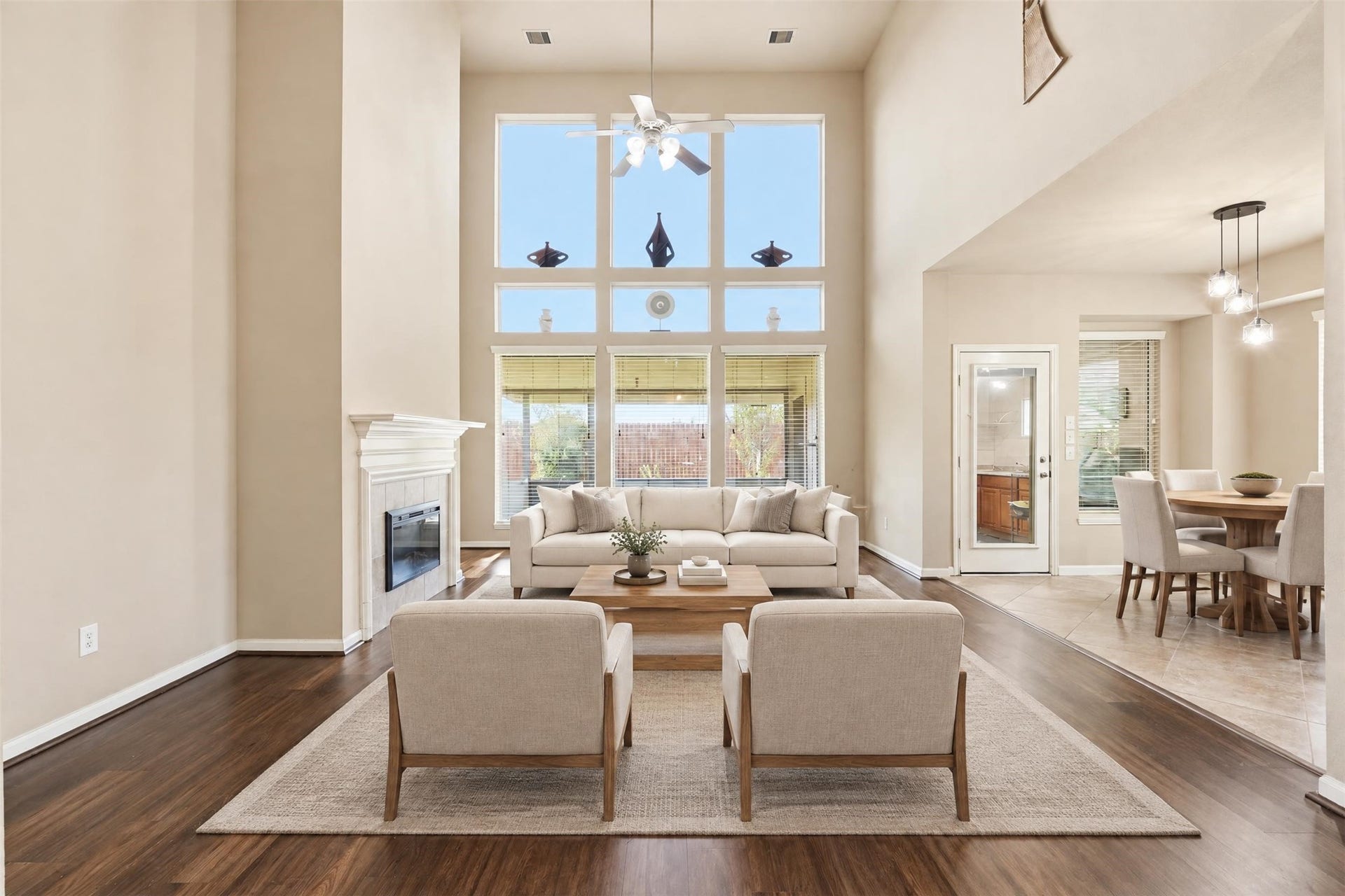 5106 Autumn Rose Lane, Sugar Land, TX 77479 Virtually staged. The two-story living room is the showpiece: a full wall of windows floods the space with natural light, and the fireplace gives the room a cozy anchor.