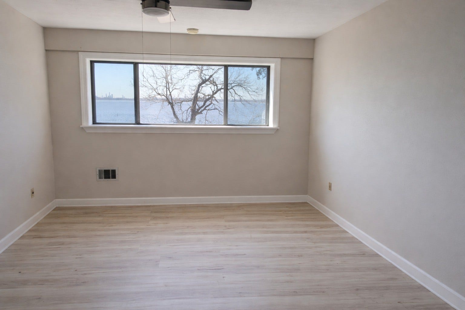Serene bedroom space highlighting soft neutral walls, durable LVP flooring, and a broad window capturing sweeping water views.