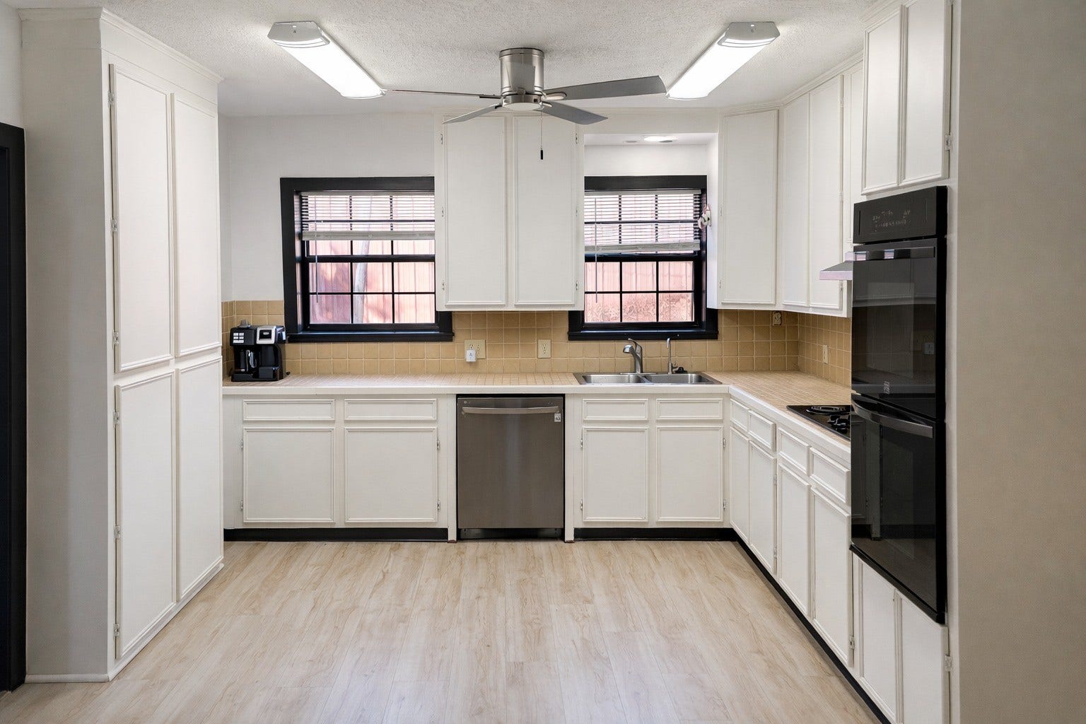 Generous kitchen space complete with bright white cabinetry, double wall ovens, ceiling fan, and durable wood-look flooring.