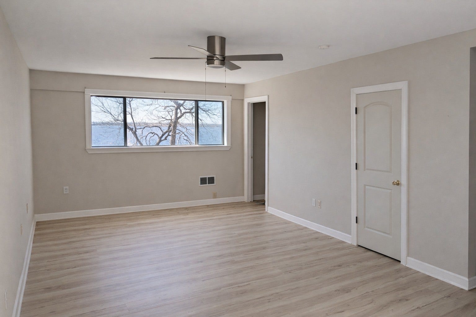 Light and airy primary bedroom featuring wood-look flooring, a modern ceiling fan, neutral wall tones, and an expansive window highlighting scenic water views.