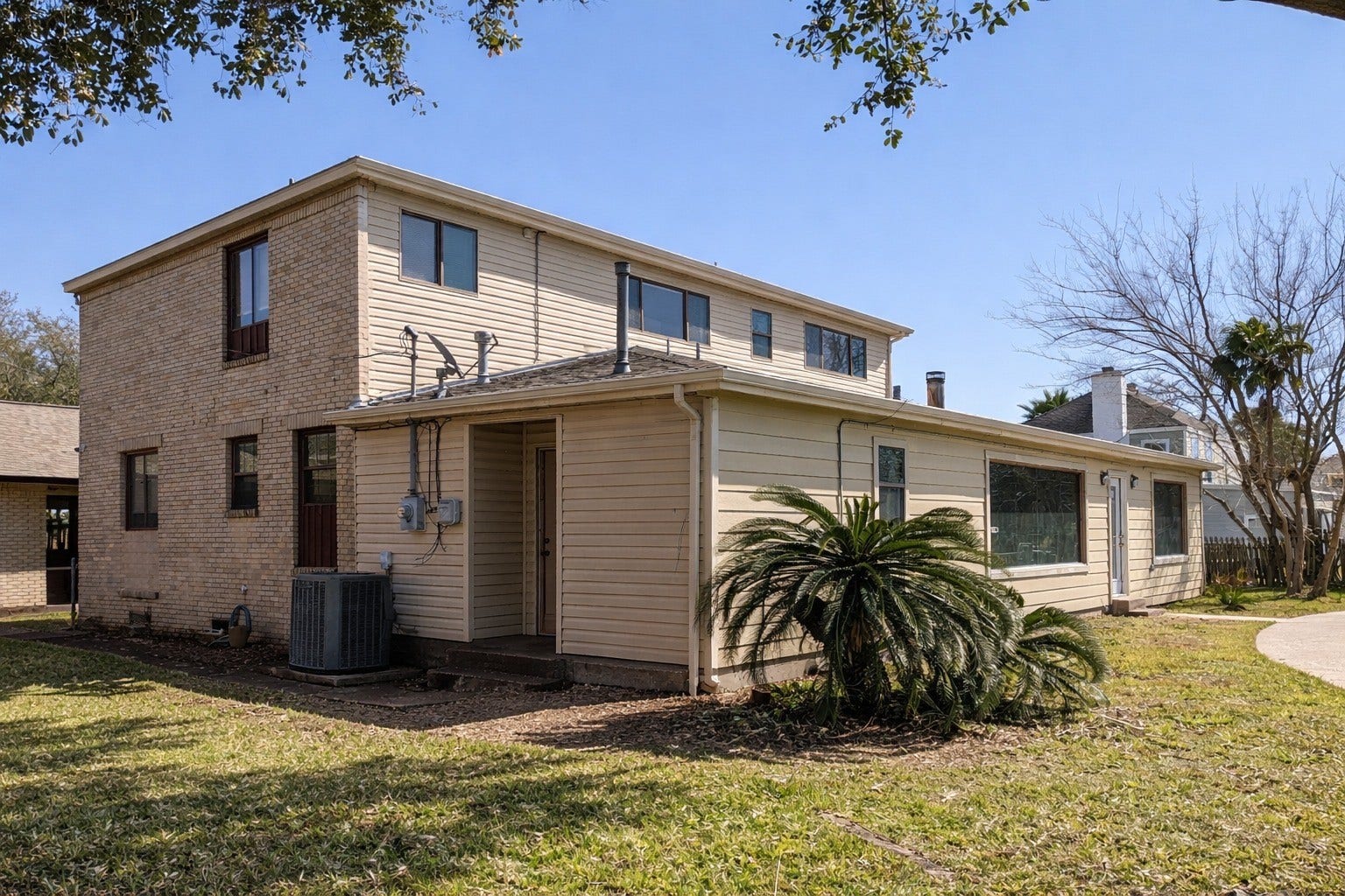 Side exterior profile displaying the two-story elevation, light siding, brick accents, and lush surrounding lawn.