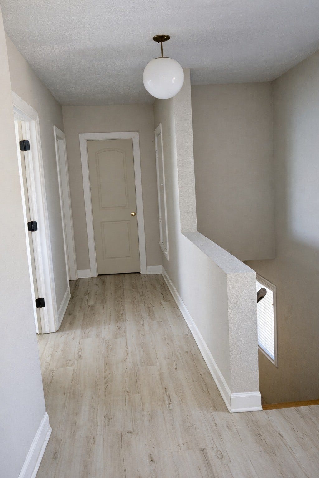 Clean upper hallway complete with modern globe pendant lighting, light wood-look flooring, and neutral wall paint.