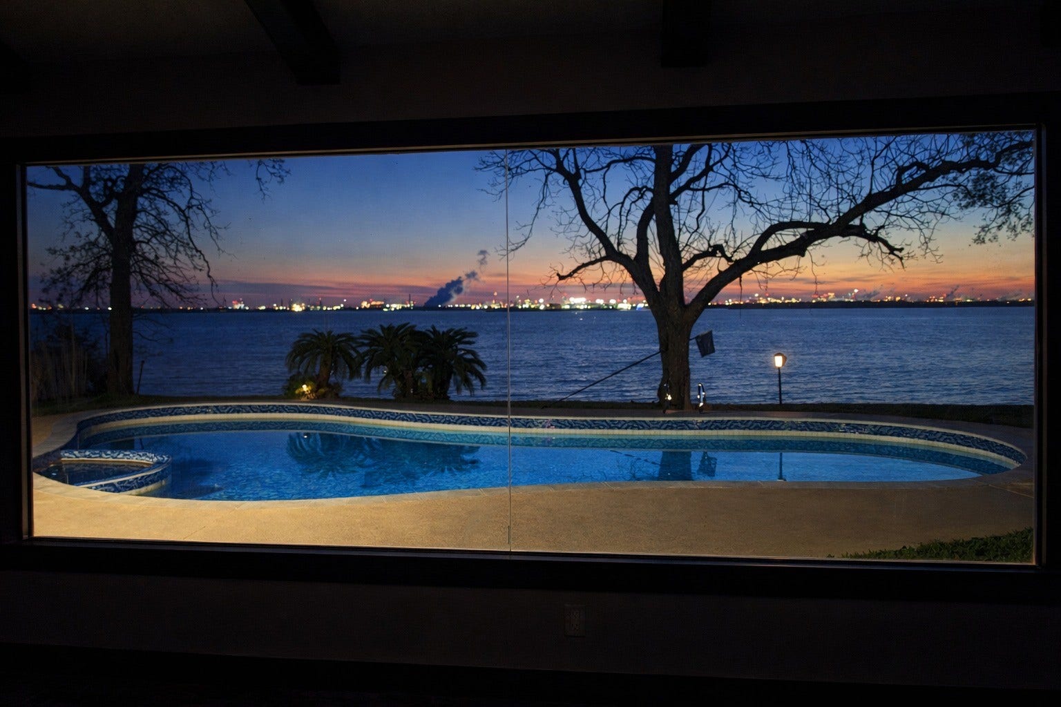 Dramatic dusk view captured through expansive picture windows, highlighting the illuminated pool, spa, and evening sky.