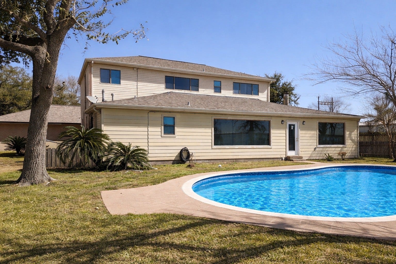 Ground-level view of the rear home elevation, sparkling in-ground pool, and surrounding green lawn.