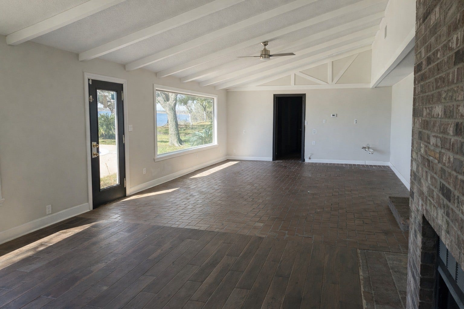 Character-filled living space featuring a vaulted beam ceiling, brick-textured flooring, a brick fireplace, and panoramic views toward the pool and water.