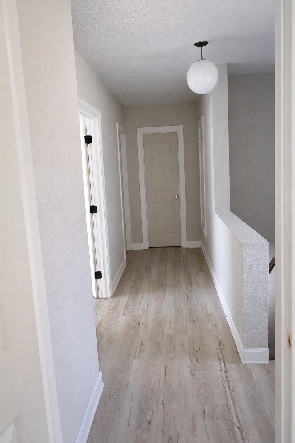 Alternate view of the upper hallway highlighting crisp white baseboards, wood-look plank flooring, and a bright, open feeling.