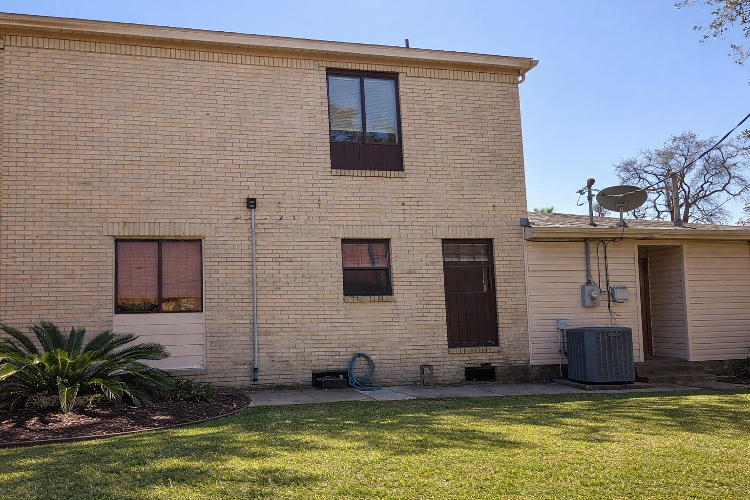 Side exterior highlighting the solid brick construction, secondary entry access, and private yard space.