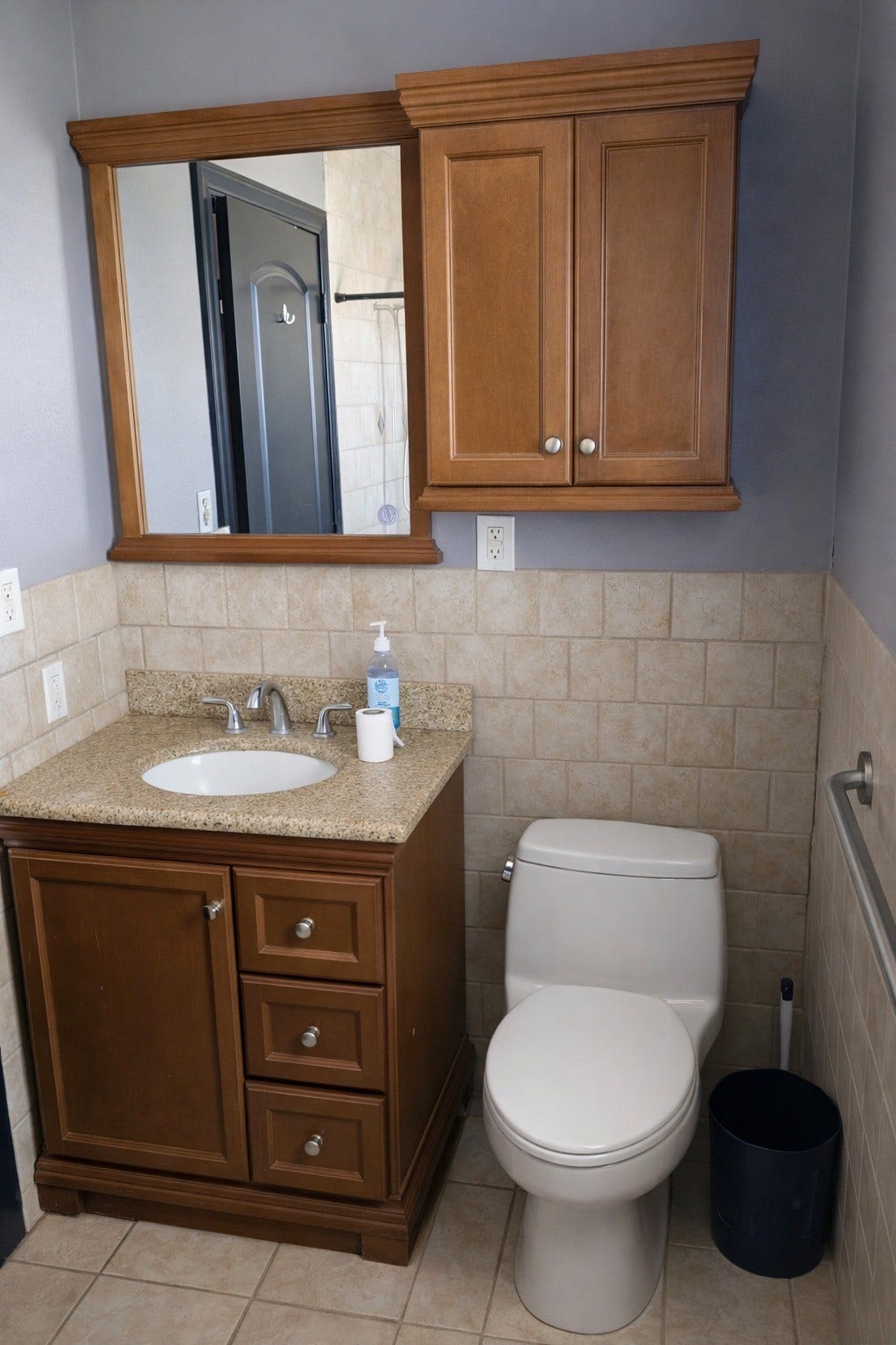Half-bathroom or secondary bath featuring a warm wood vanity, upper storage cabinet, tiled wainscoting, and neutral finishes.