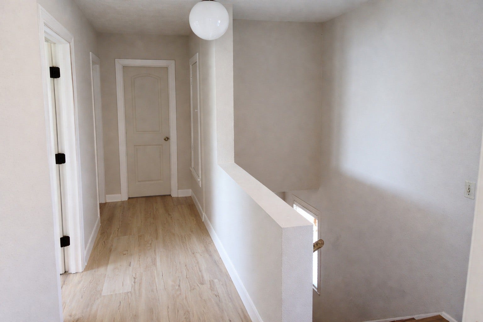 Clean upper hallway featuring fresh neutral paint, light LVP flooring, a contemporary globe lighting fixture, and a low partial wall along the stairwell.