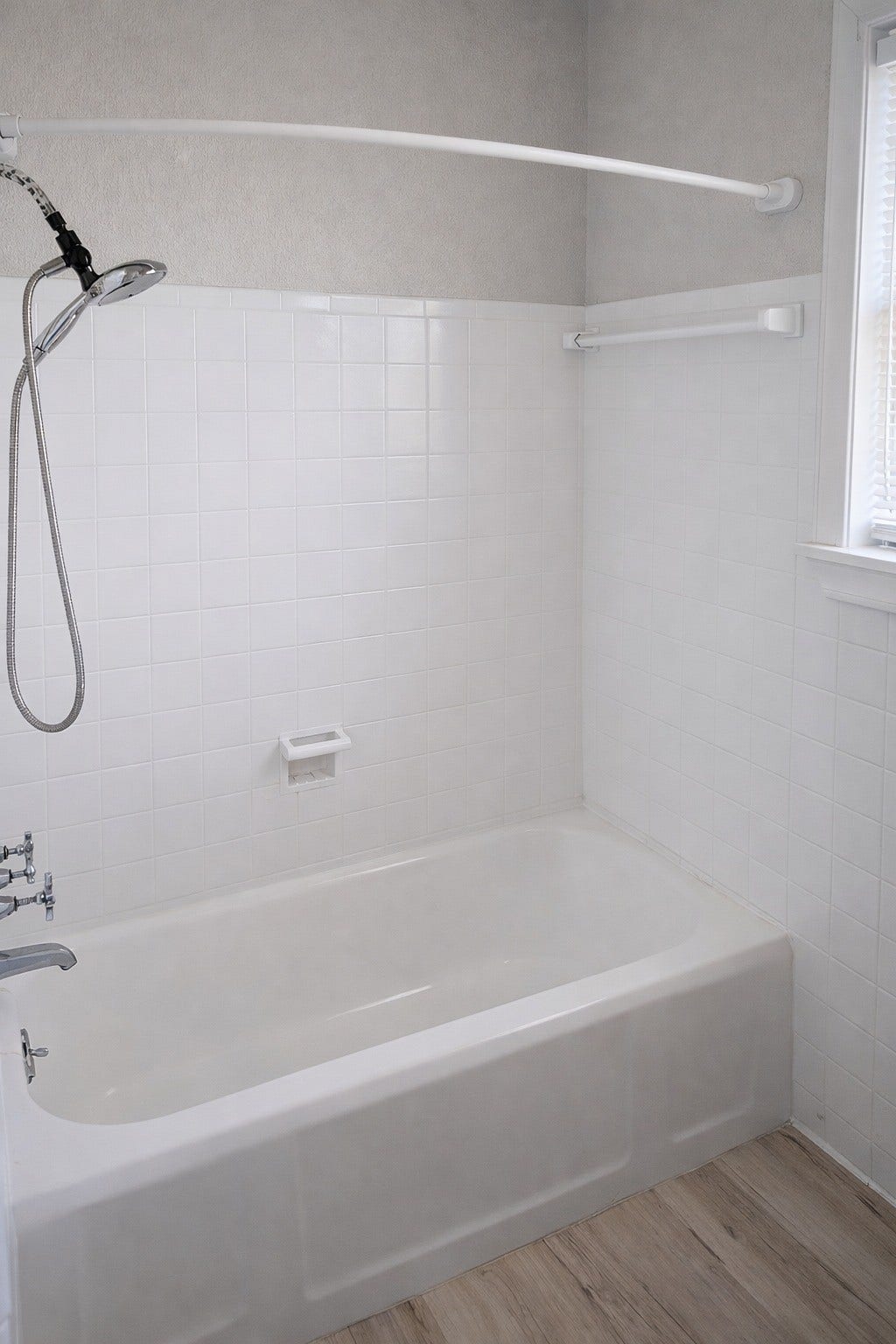Classic full bathroom complete with a soaking tub/shower combination, crisp white subway tile surround, and light wood-look flooring.