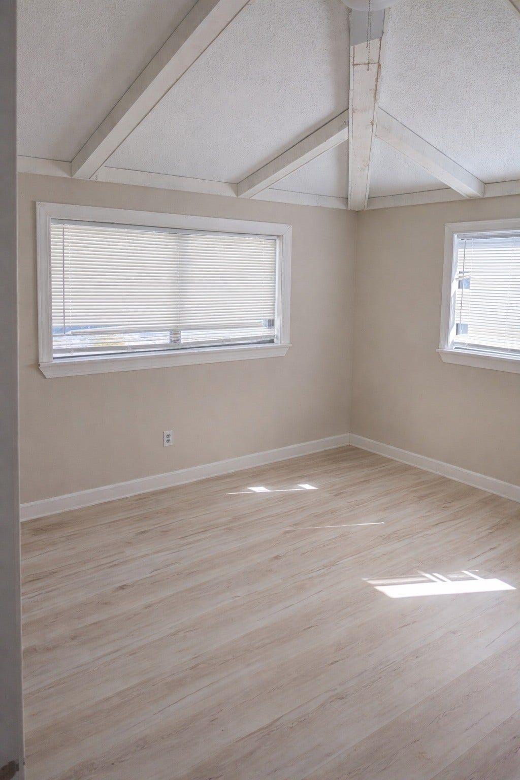 Airy room with vaulted beam ceilings, light-colored plank flooring, crisp white trim, and multiple sunlit windows.
