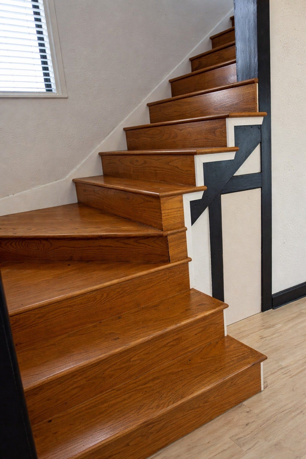 Custom architectural staircase featuring rich hardwood treads, contrasting dark trim accents, and natural lighting from a nearby window.