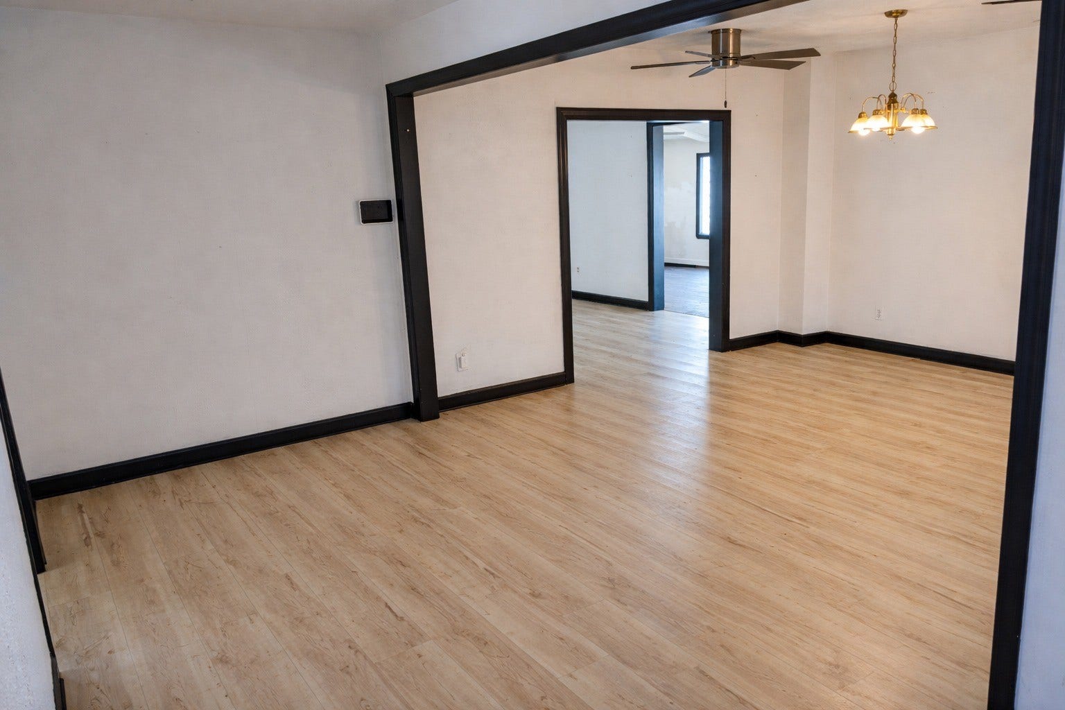 Broad living space demonstrating seamless flow between rooms, framed by distinct dark-trimmed architectural passageways and modern flooring.