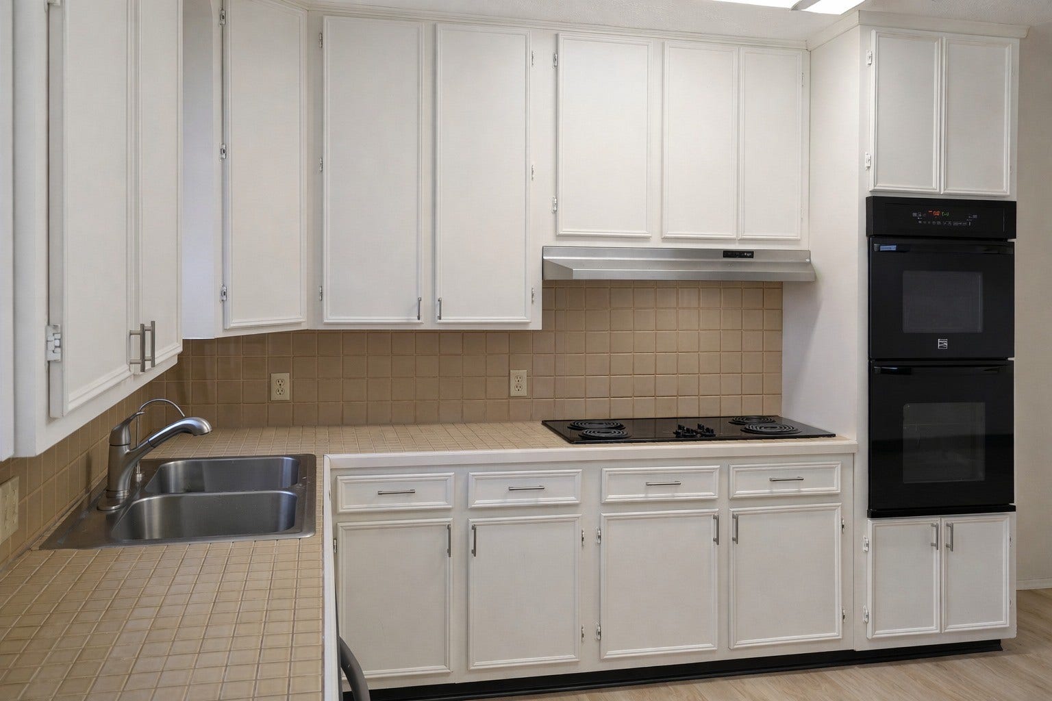 Alternate angle of the functional kitchen highlighting abundant white cabinet storage, double sink, electric cooktop, and built-in ovens.