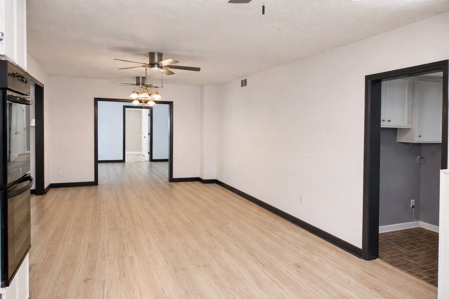 Expansive primary living area with wood-look flooring, twin ceiling fans, classic light fixtures, and prominent dark trim doorways.