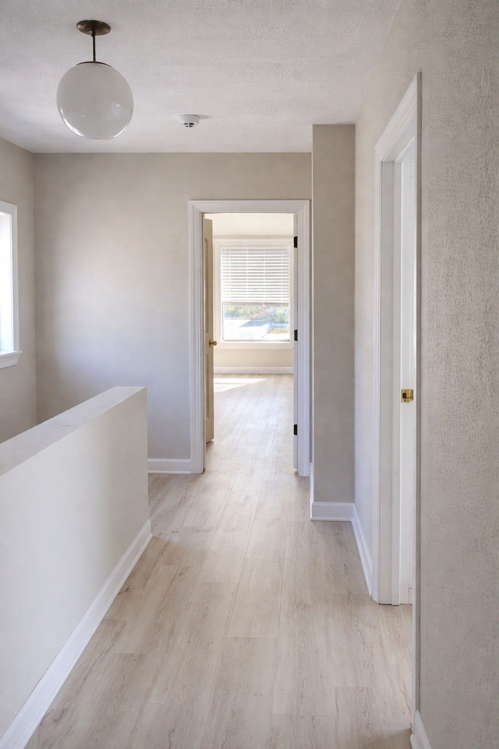 Upper-level hallway featuring seamless wood-look flooring, crisp white trim, globe pendant lighting, and easy access to neighboring rooms.