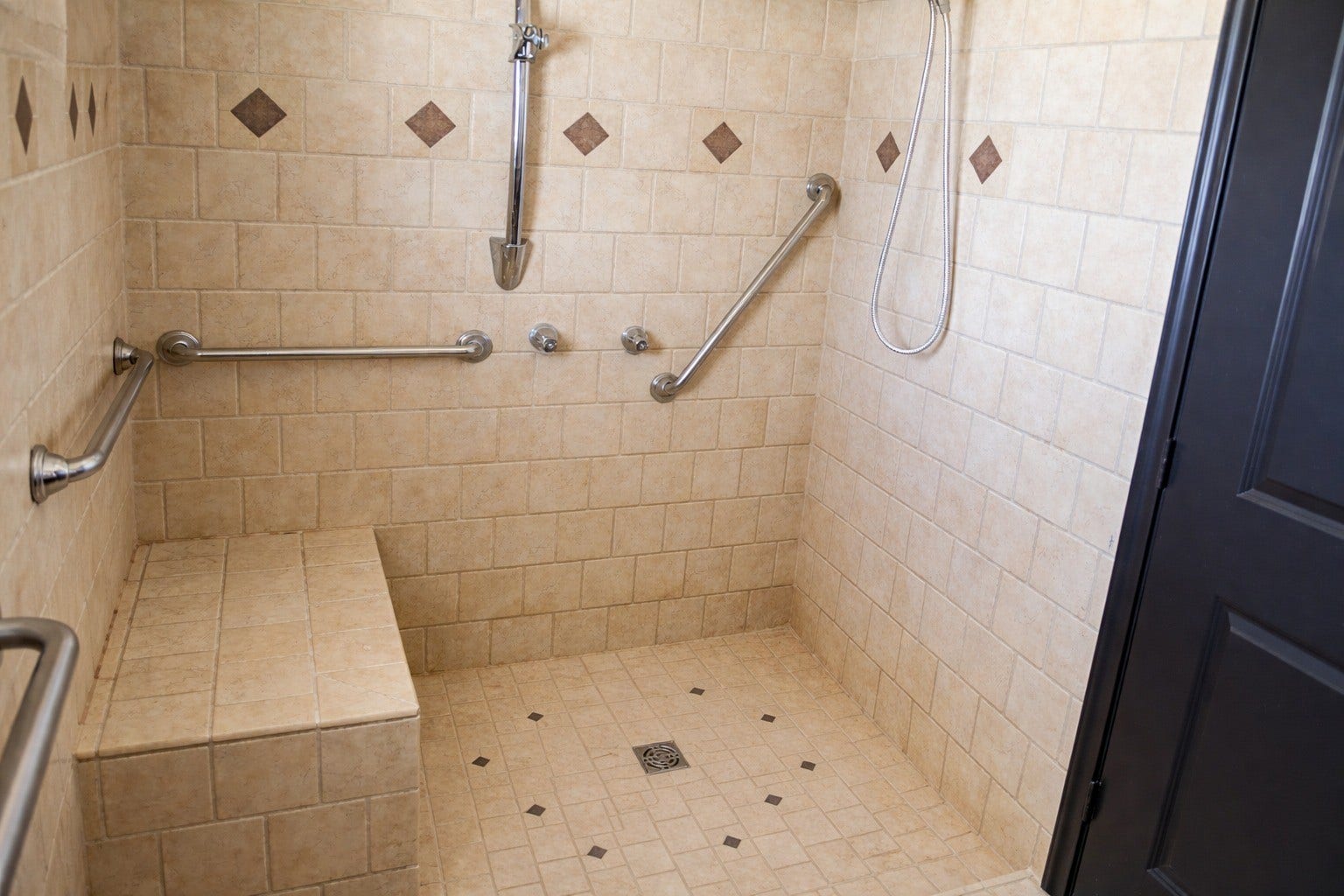 Accessible walk-in primary shower complete with full tile surround, built-in seating bench, safety grab bars, and multiple showerheads.