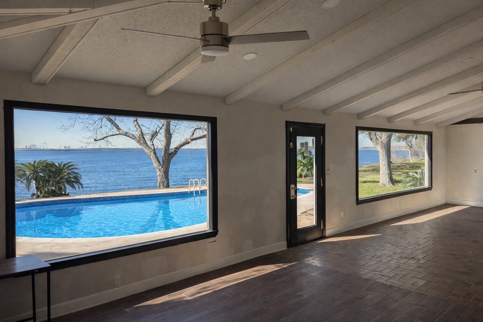 Bright sunroom addition boasting vaulted ceilings, ceiling fan, and massive picture windows overlooking the sparkling pool and open bay waters.