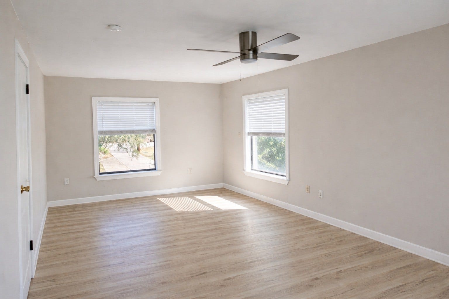 Bright corner bedroom with double-aspect windows, soft light-wood flooring, neutral trim, and a modern overhead ceiling fan.