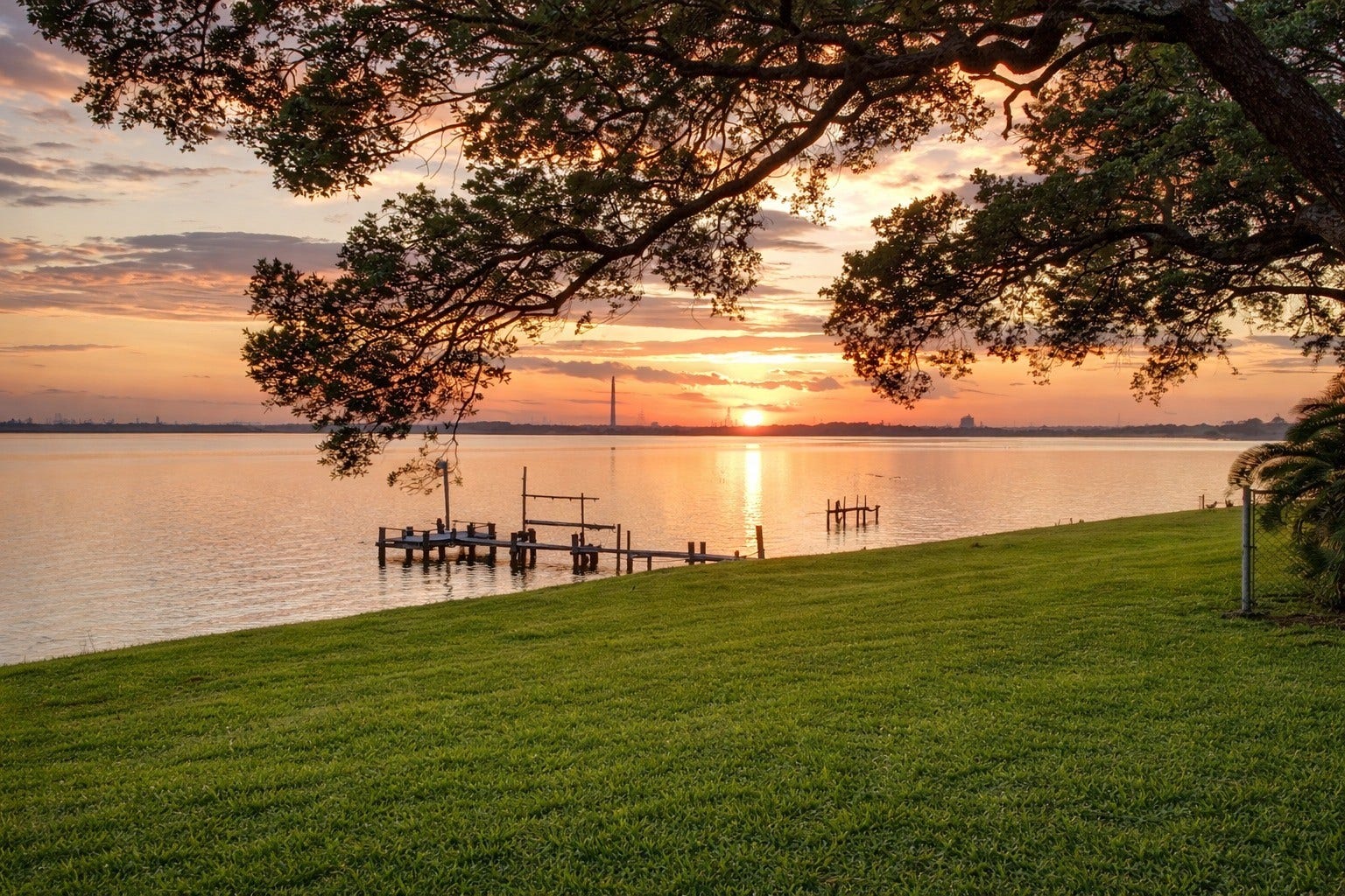 Picturesque sunset scene framing the sprawling green lawn, private pier/dock, and peaceful open bay water.