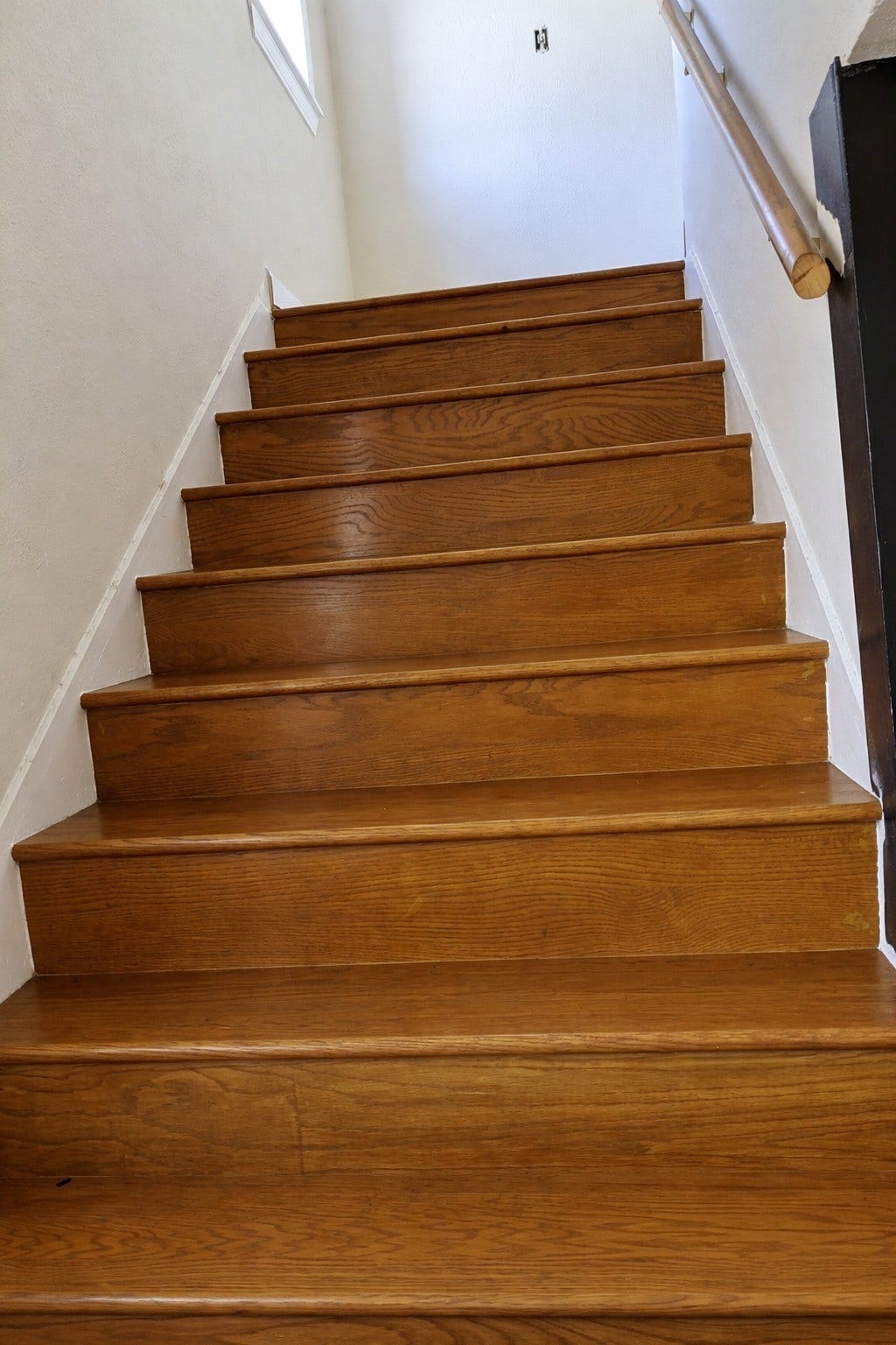 Classic interior wooden staircase with warm hardwood treads, a sturdy handrail, and a clean white riser contrast.