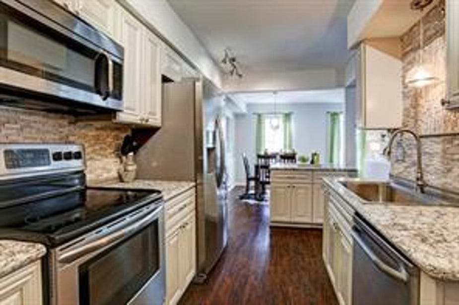 This kitchen features modern stainless-steel appliances, granite countertops, and a stylish backsplash. It opens into a cozy dining area with natural light, creating an inviting and functional space.
