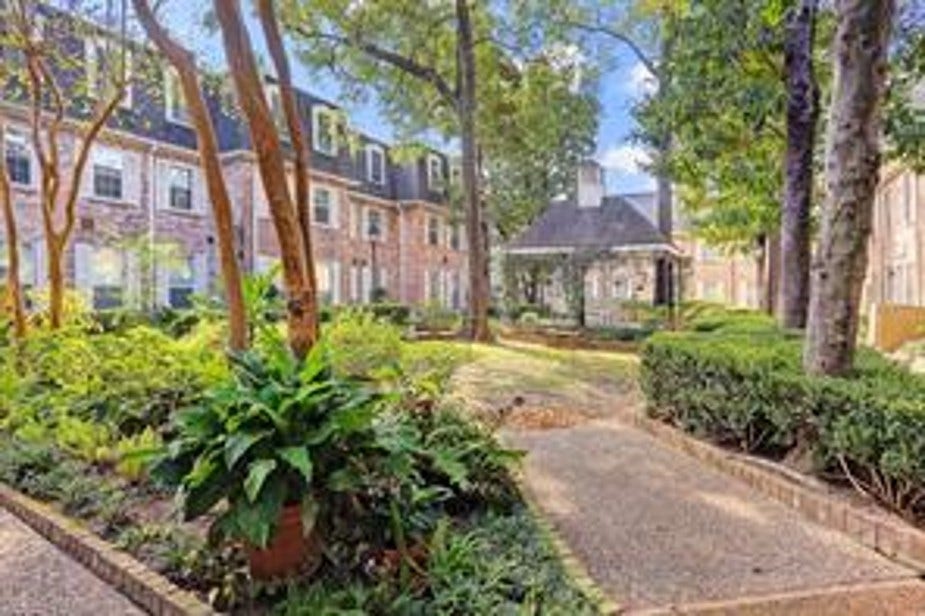 Lush courtyard view with greenery, mature trees, a community grill and a quaint gazebo. Surrounded by classic brick style with white-framed windows, has the feel of a European village. Creating a serene and inviting atmosphere.