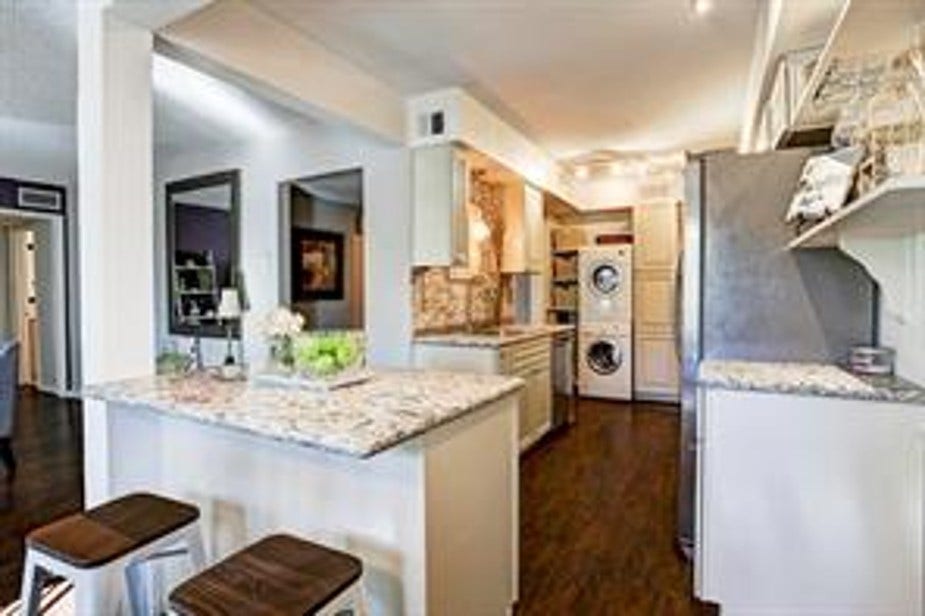 Open concept kitchen with granite countertops, a breakfast bar, accommodating two stools. It features ample cabinetry, and a in unit stacked washer and dryer. The space is open and well-lit, with a view into dining and living.