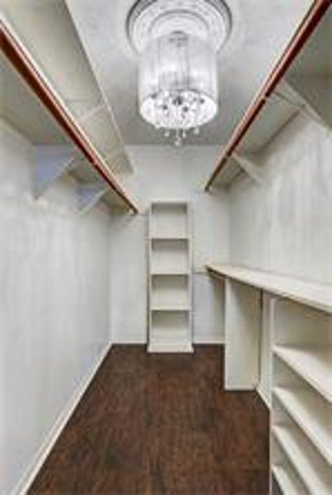This spacious walk-in closet features elegant wooden flooring, ample shelving, and hanging space, highlighted by a stylish chandelier for a touch of luxury.