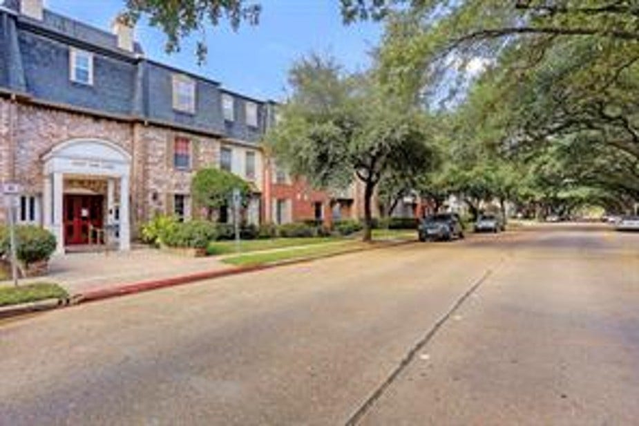 This photo shows a charming townhouse with a classic brick exterior located on a tree-lined street. The area is peaceful and well-maintained, offering guest parking on both sides of the street. The canopy of trees makes it one of the most beautiful streets in the area.