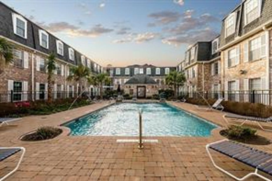 Lush courtyard view with greenery, mature trees, a community grill and a quaint gazebo. Surrounded by classic brick style with white-framed windows, has the feel of a European village. Creating a serene and inviting atmosphere.