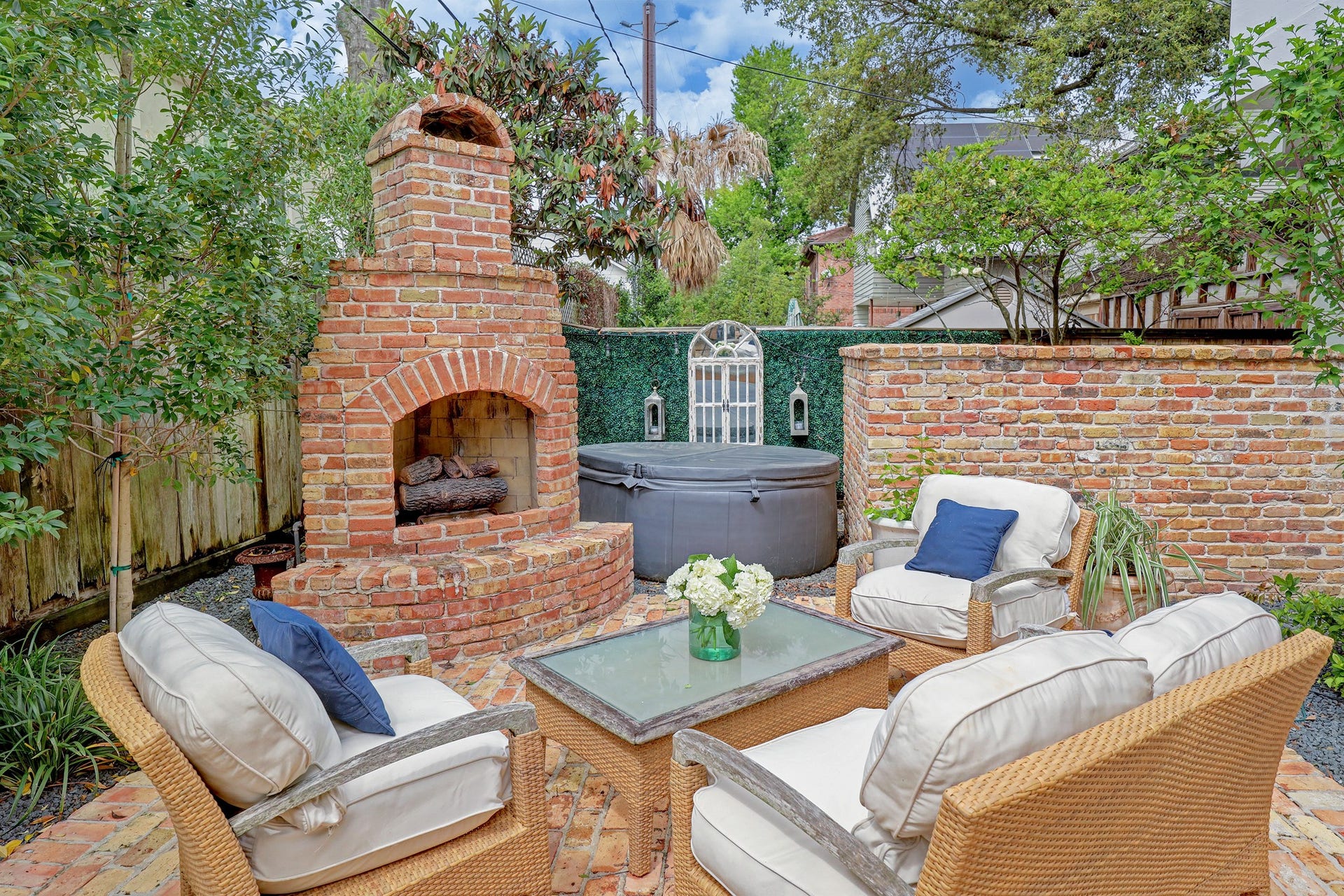 6004 Lake Street, Houston, TX 77005 Charming outdoor retreat featuring a classic brick fireplace, cozy seating area with cushioned chairs (hot tub has been removed), all surrounded by lush greenery for privacy and ambiance.