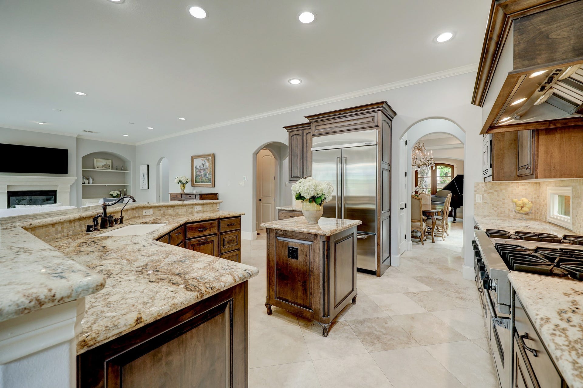 6004 Lake Street, Houston, TX 77005 Spacious gourmet kitchen with abundant countertops, custom wood cabinetry, and a large stainless steel refrigerator. The room flows seamlessly into family room with a fireplace, perfect for entertaining.