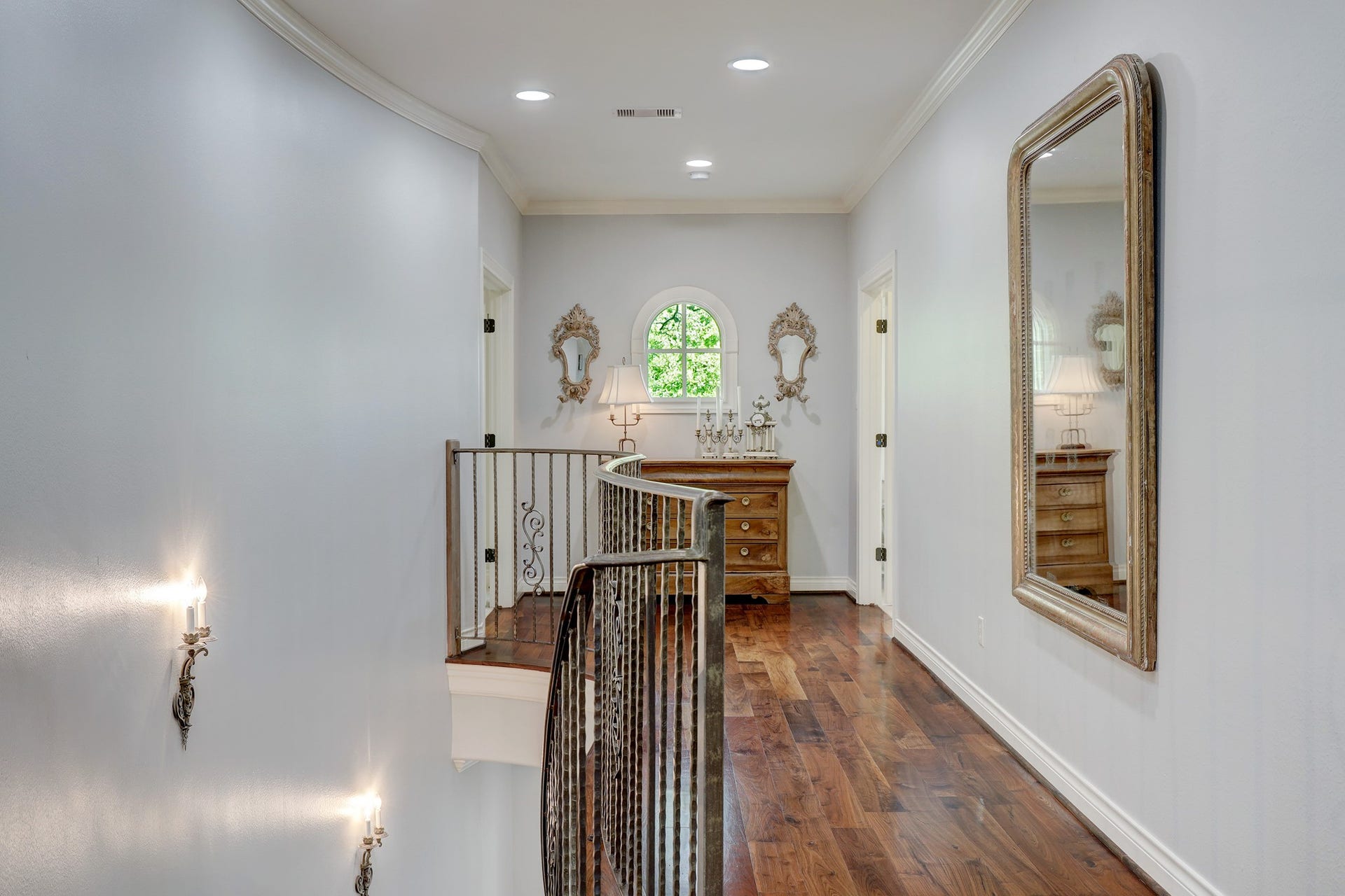 6004 Lake Street, Houston, TX 77005 The second-floor landing hallway features rich hardwood flooring, ornate wall sconces, and a gracefully curved staircase railing.