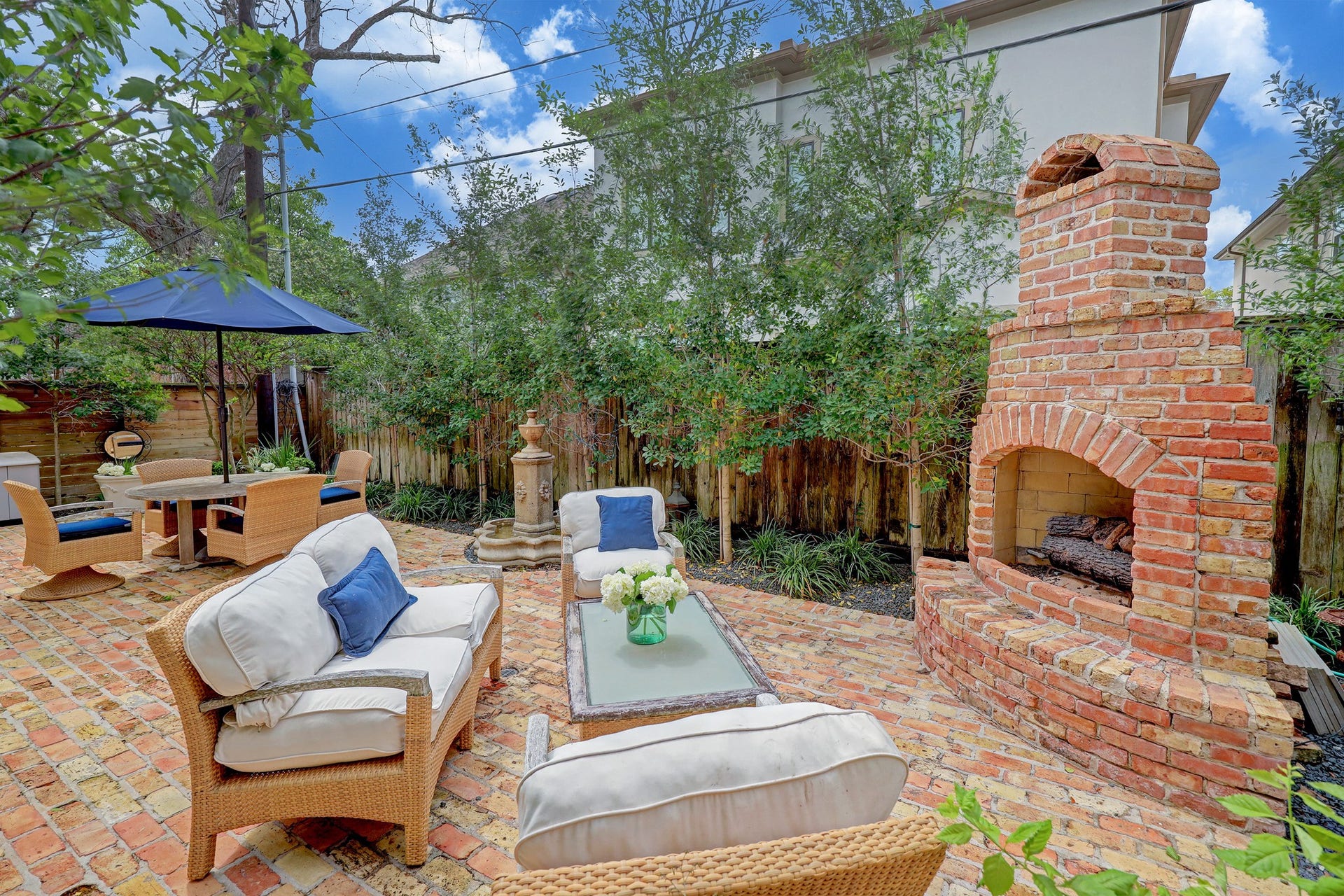 6004 Lake Street, Houston, TX 77005 Charming outdoor retreat featuring a brick patio with a cozy fireplace, ample seating, and lush greenery for a perfect relaxation spot.