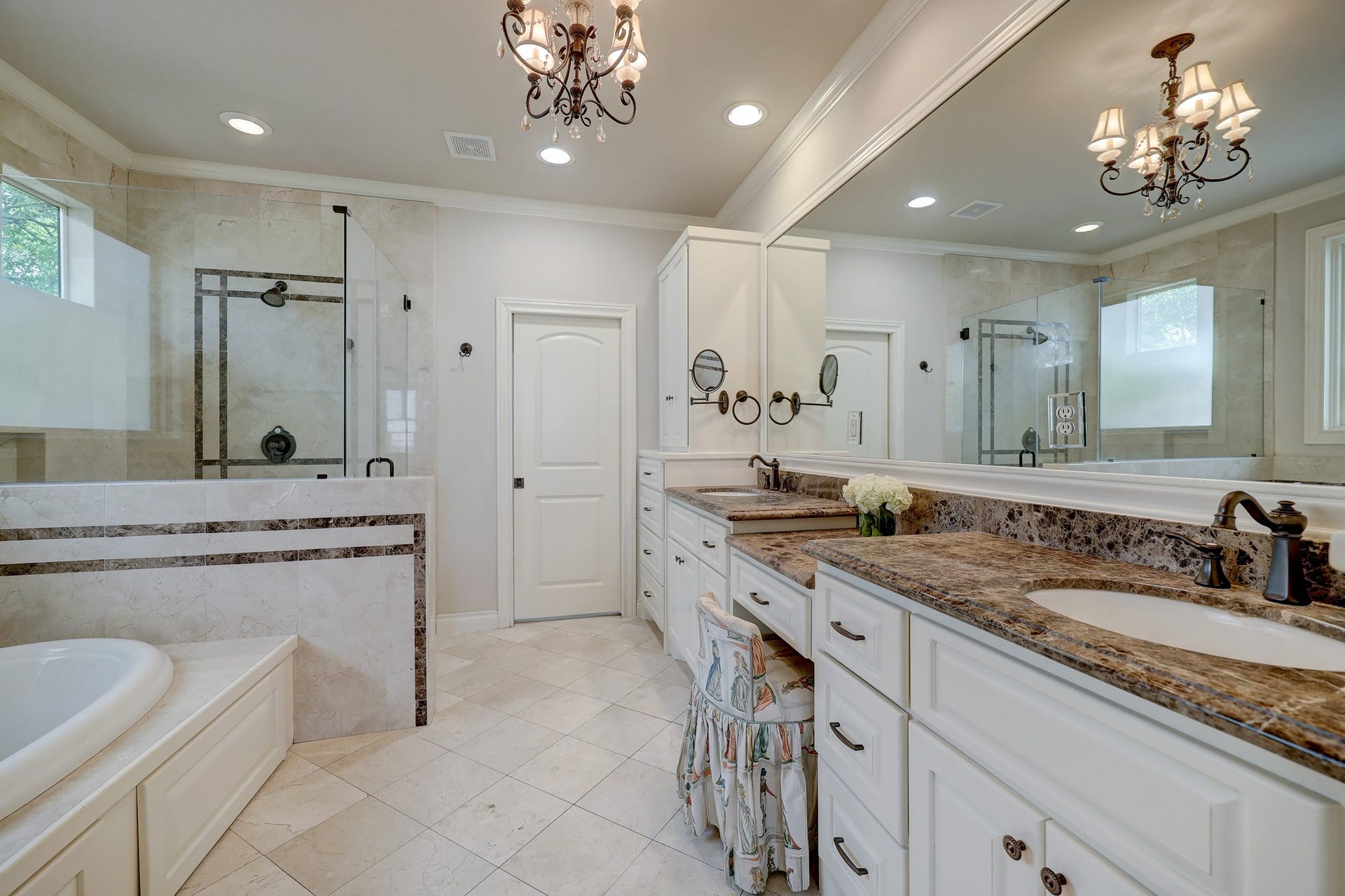 6004 Lake Street, Houston, TX 77005 The primary bathroom features a dual vanity with double-sink countertops, a luxurious soaking tub, and a spacious glass-enclosed shower, all lit by a stylish chandelier.