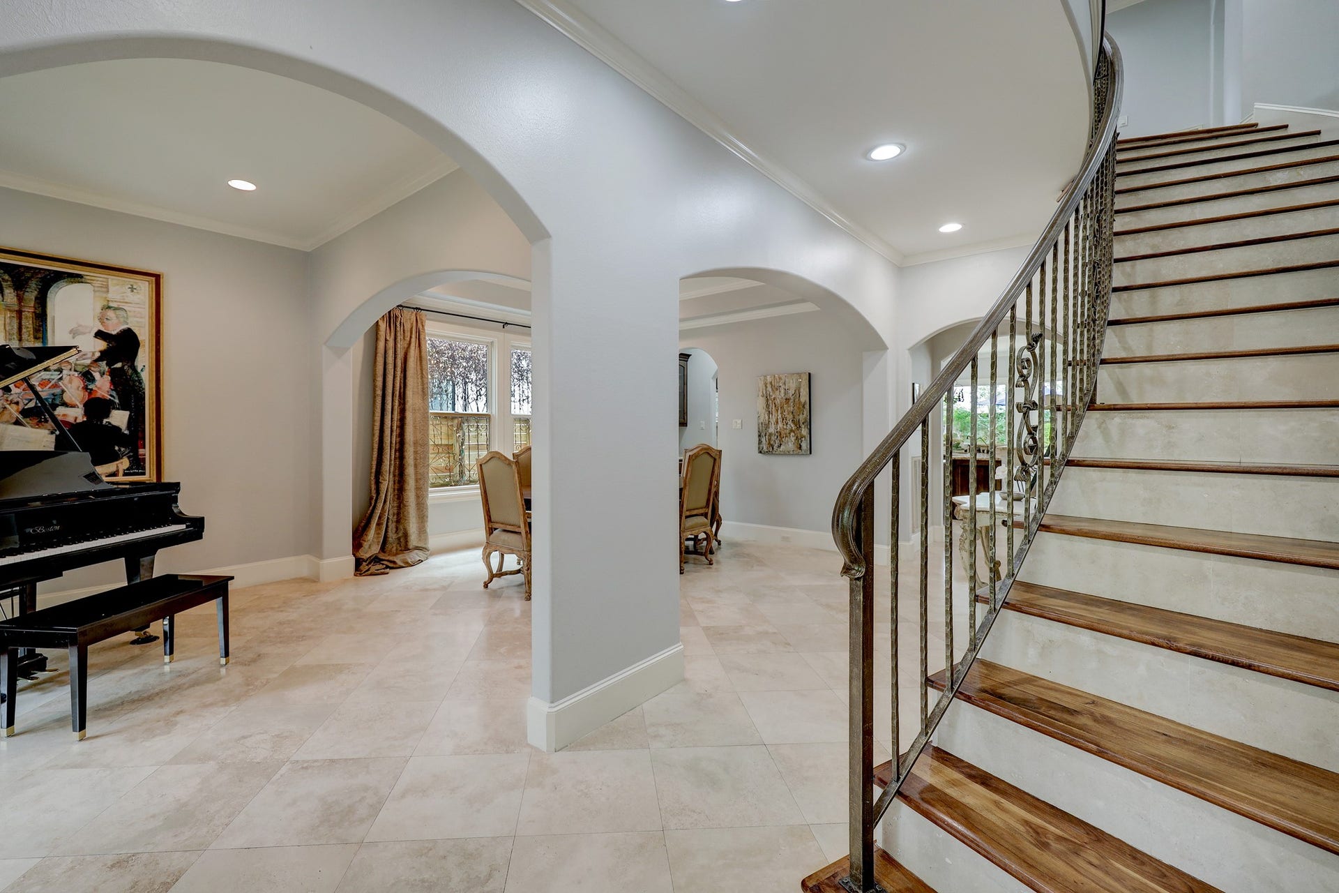 6004 Lake Street, Houston, TX 77005 Elegant entryway featuring a grand staircase with wrought iron railings, leading to a spacious living area with a grand piano and arched doorways.