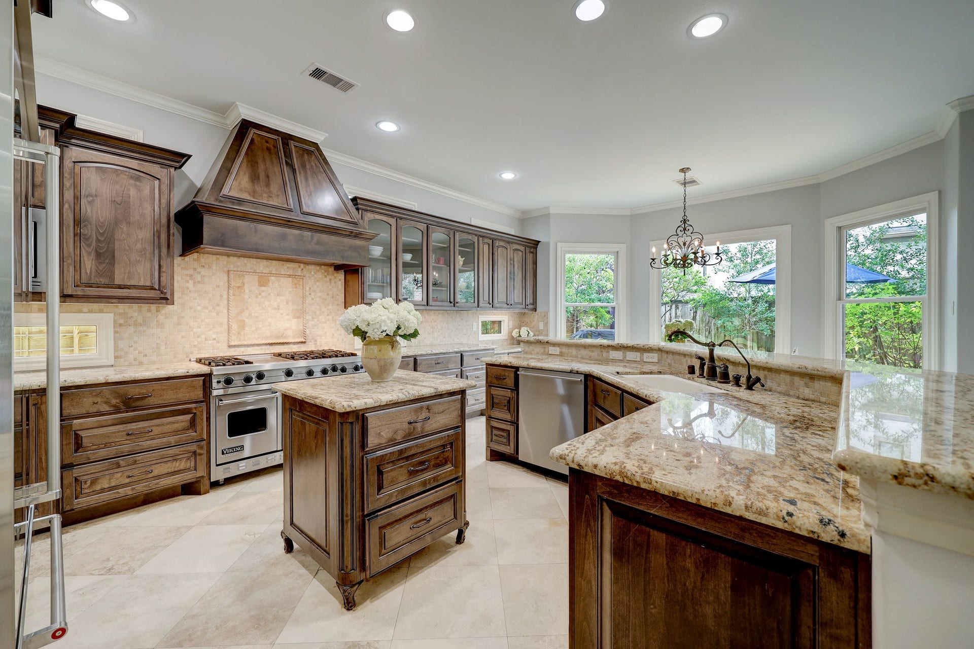 6004 Lake Street, Houston, TX 77005 This kitchen offers rich wood cabinetry, spacious countertops, and a central island. Equipped with a high-end range and stainless steel appliances, it features large windows offering a bright and inviting space.