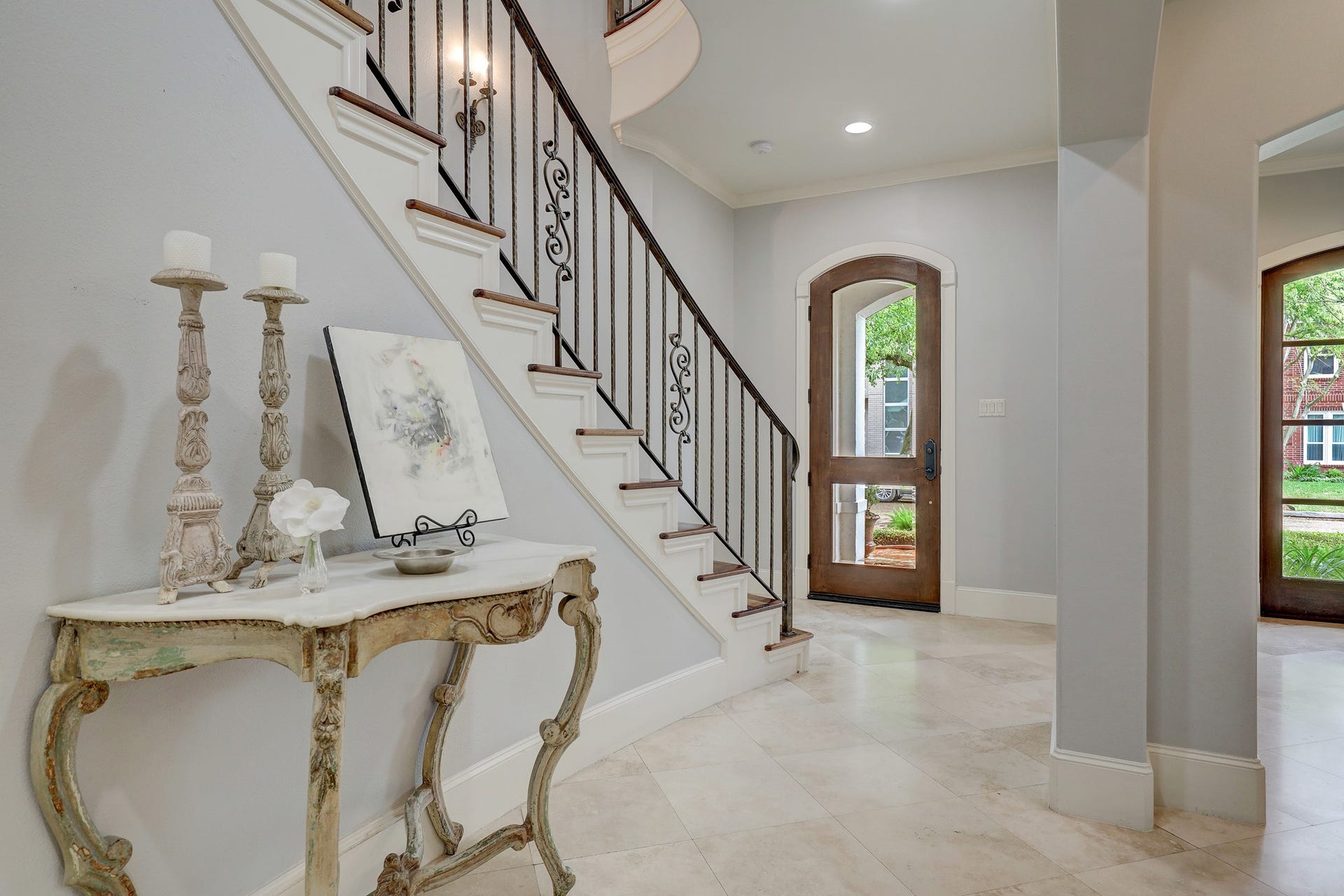 6004 Lake Street, Houston, TX 77005 Elegant entryway featuring a graceful staircase with wrought iron railings, complemented by travertine floors leading to a beautiful wooden front door.