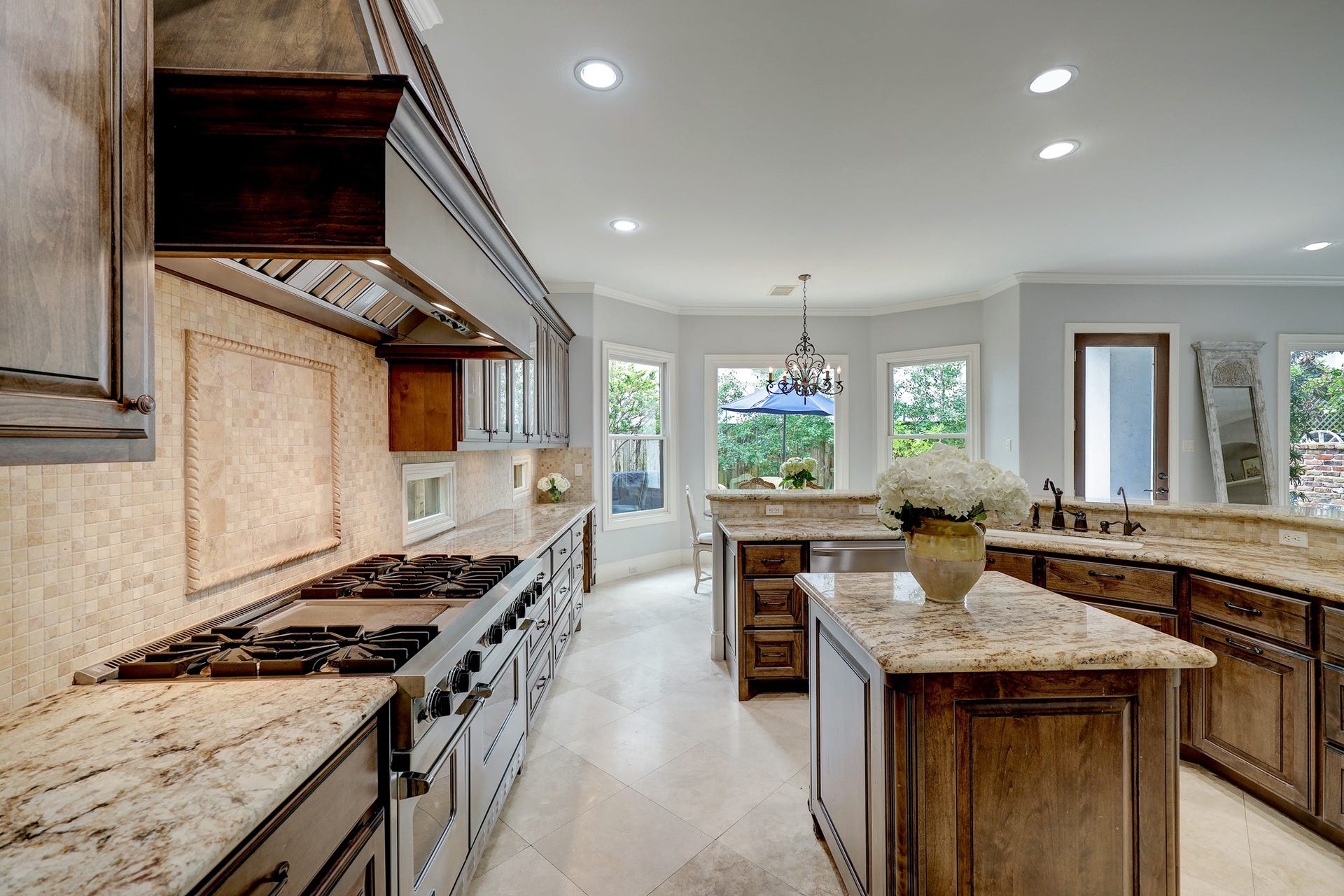 6004 Lake Street, Houston, TX 77005 Spacious gourmet kitchen featuring a cook's dream in countertop space, custom wood cabinetry, and a large gas range. Natural light floods in through bay windows, highlighting the central island and breakfast seating bar. Perfect for culinary enthusiasts.