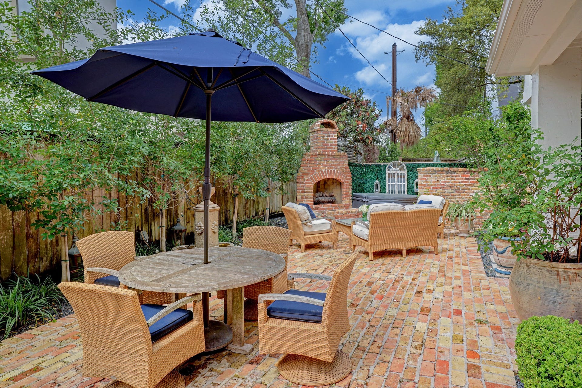 6004 Lake Street, Houston, TX 77005 Charming outdoor patio featuring a cozy seating area, brick fireplace, and dining table with umbrella, perfect for entertaining and relaxation.